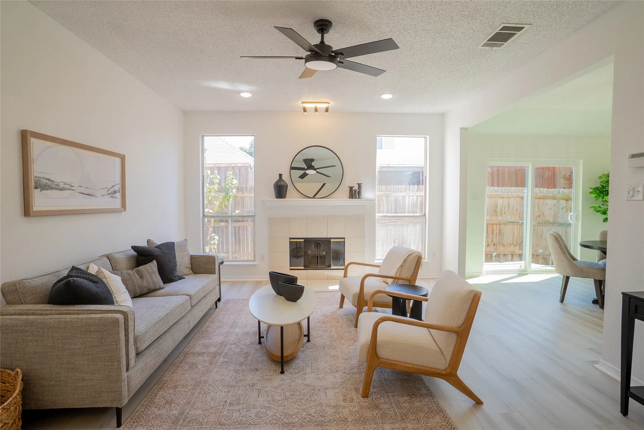 Bright living space with wood-finish flooring, a contemporary ceiling fan, and a tiled fireplace