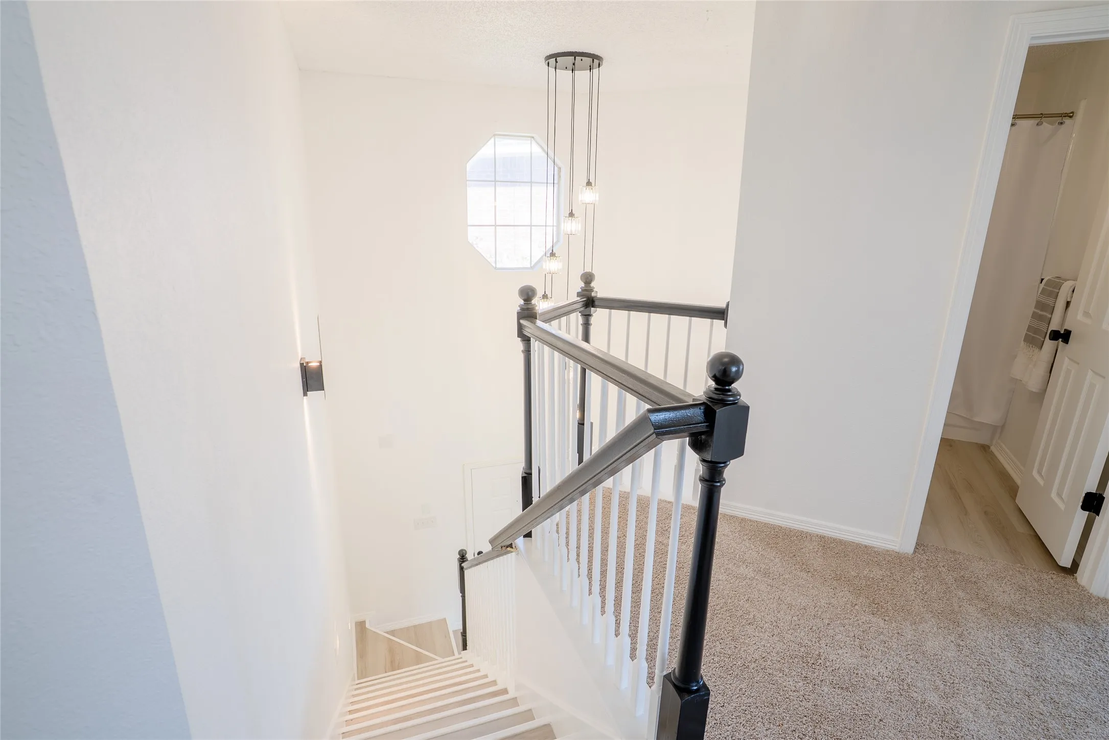 Staircase featuring wood-finish treads and risers, a black and white balustrade, and a multi-pendant light fixture