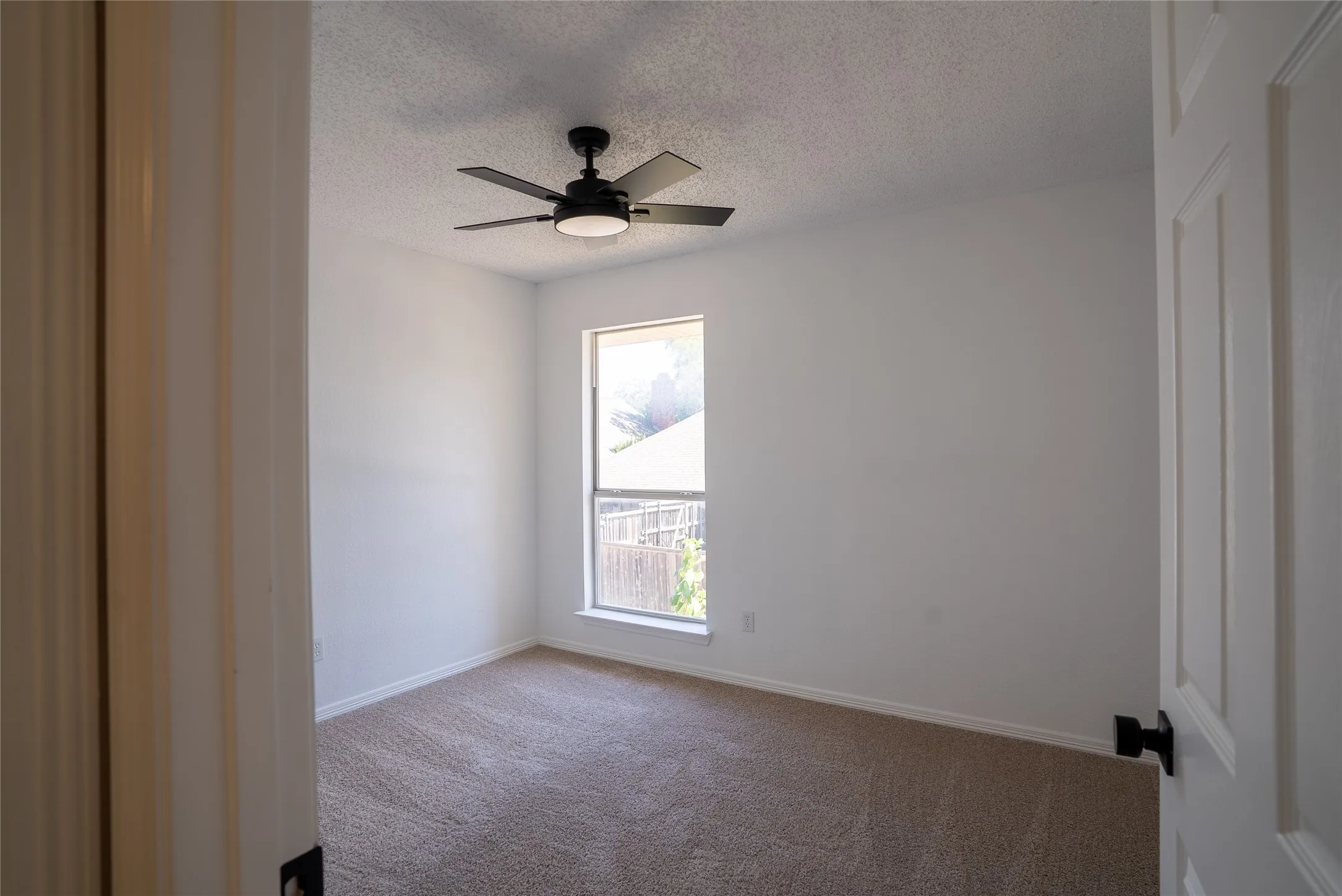 Recessed window with exterior fencing, ceiling fan with integrated lighting, and carpeted flooring