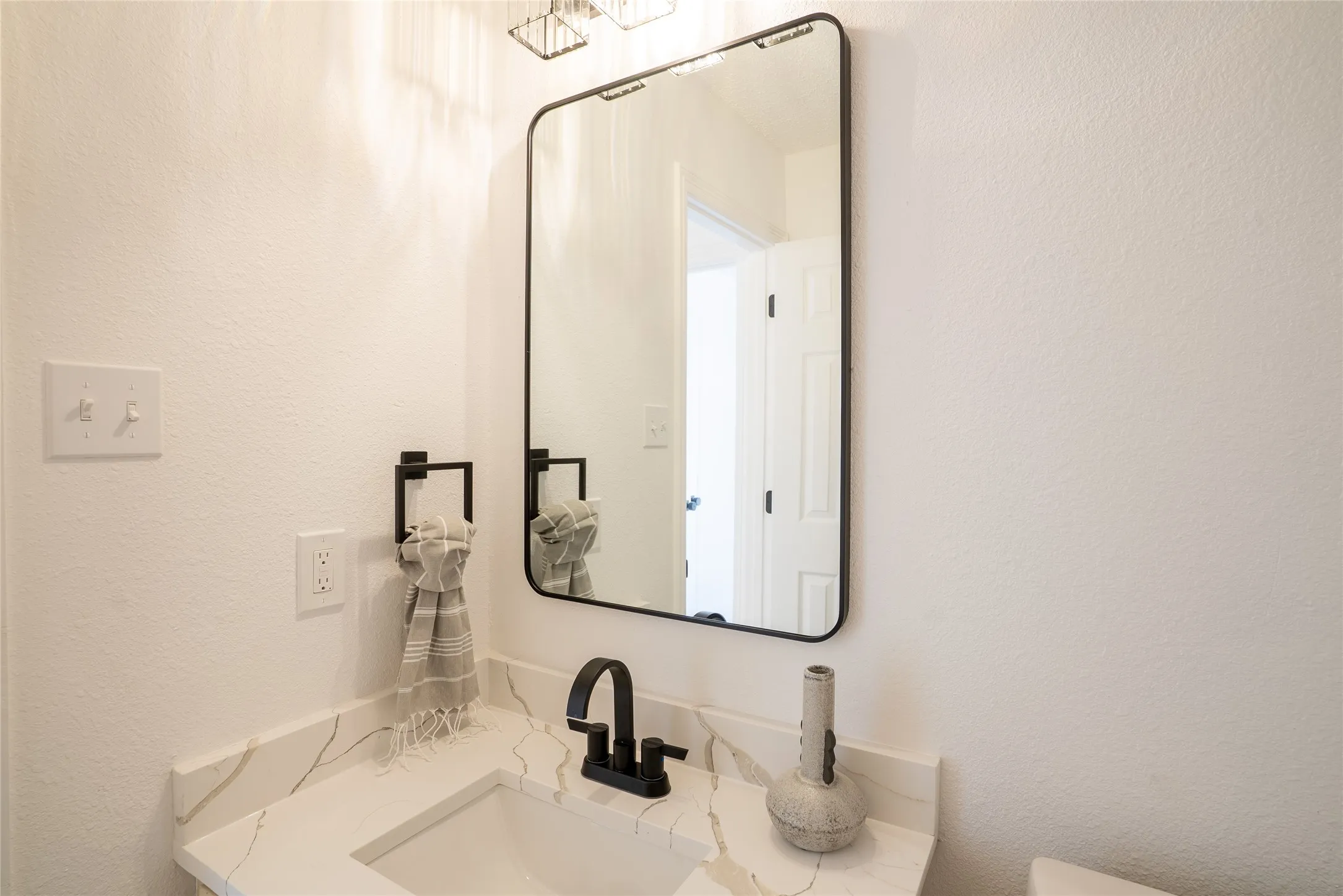 White quartz countertop with veining, integrated rectangular sink, matte black faucet, and a black-framed mirror