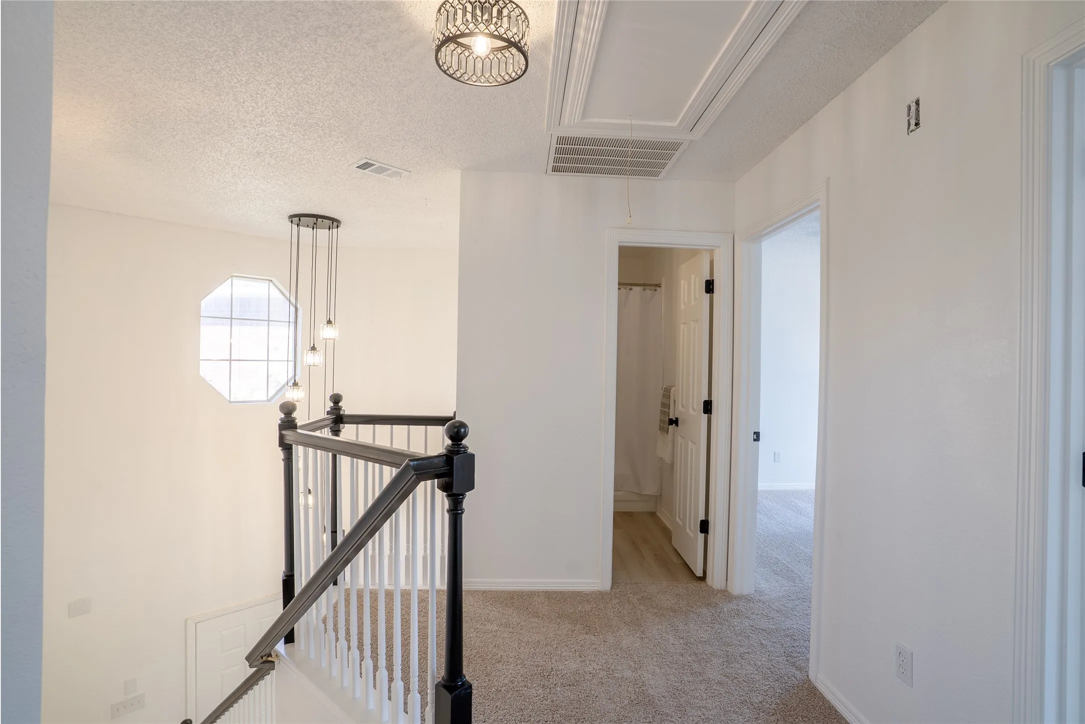 Octagonal window, black and white staircase railing, carpeted flooring, two panel doors, and a decorative semi-flush mount light fixture