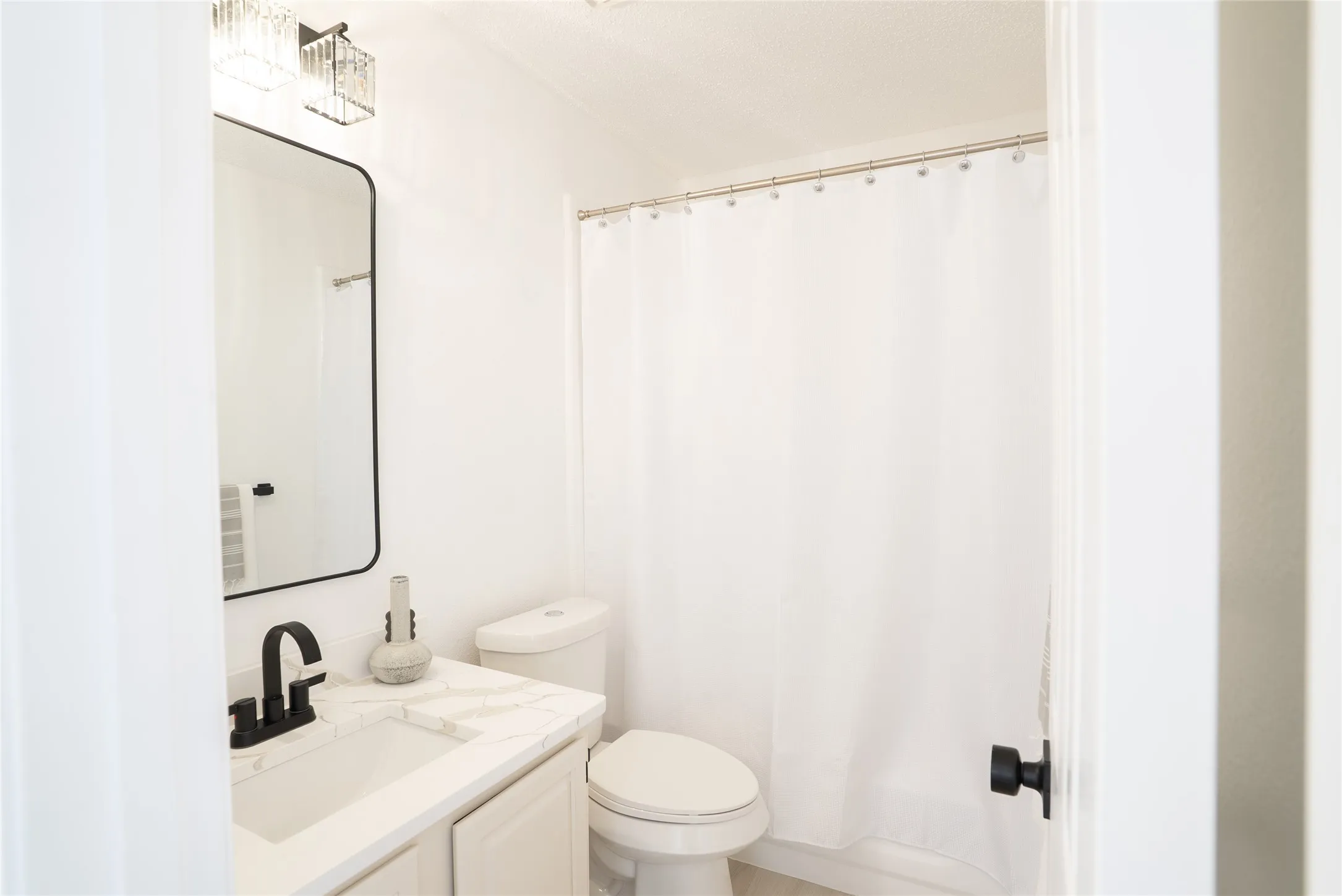 White vanity with a rectangular undermount sink, matte black faucet, and stone-finish countertop