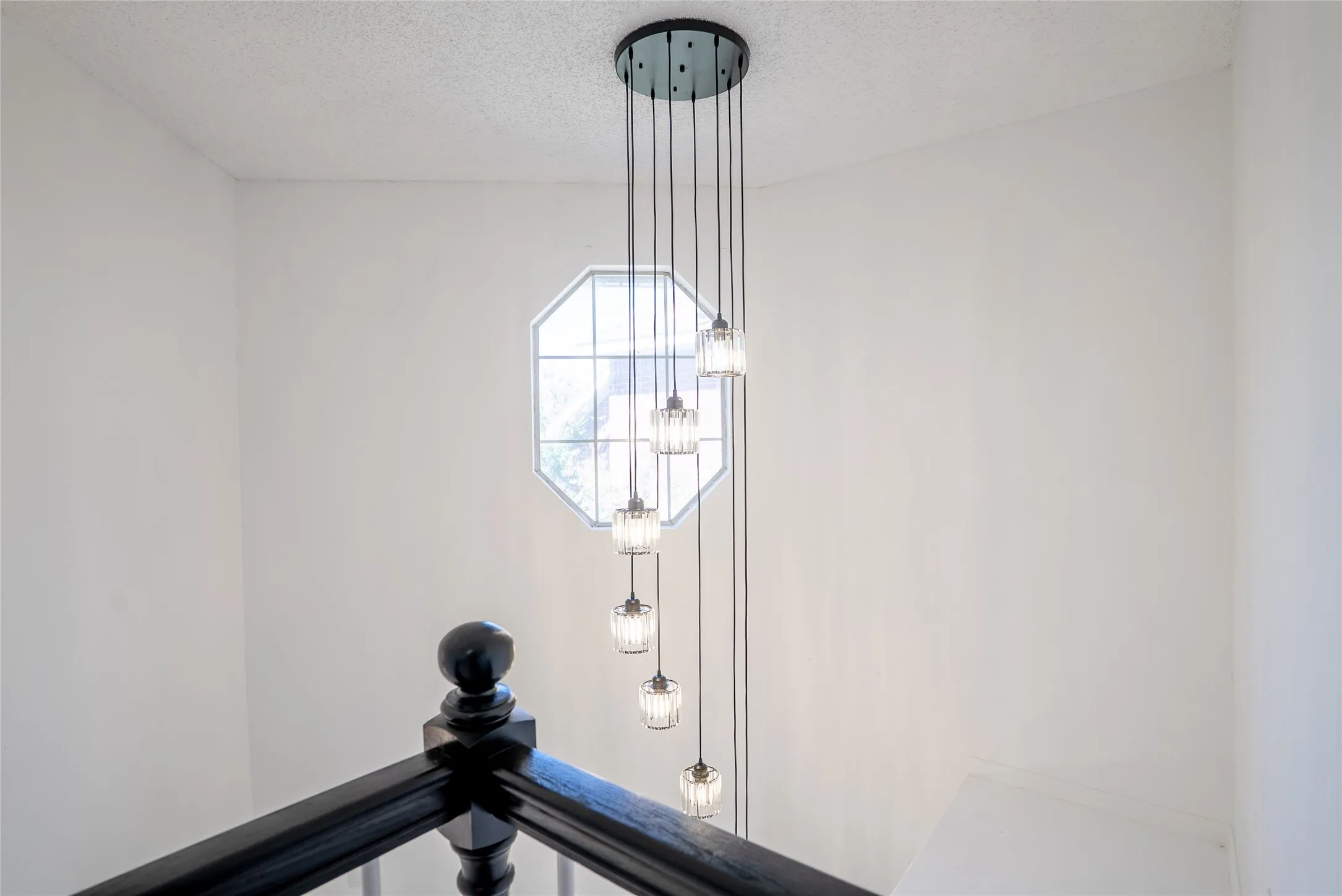 Octagonal window, multi-light pendant fixture, white wall finish, painted wood handrail, painted wood newel post