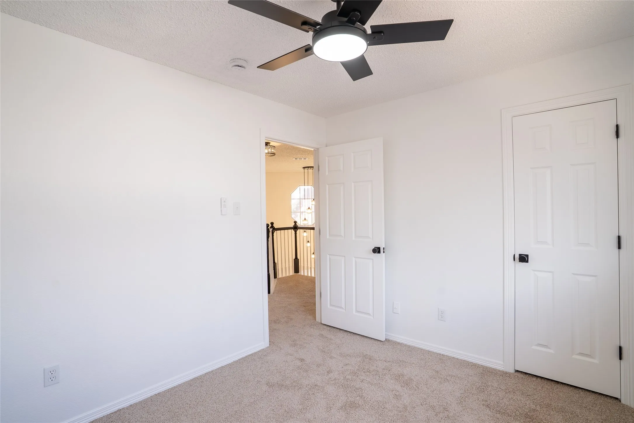 Plush carpeting, crisp white walls, contemporary ceiling fan with integrated lighting, and multiple paneled doors with matte black hardware