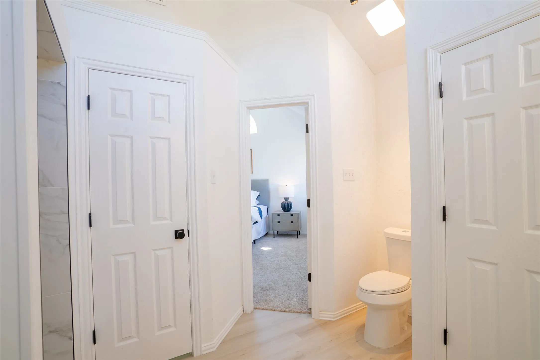 Light-toned wood-finish flooring, white paneled doors with dark hardware, and a white toilet