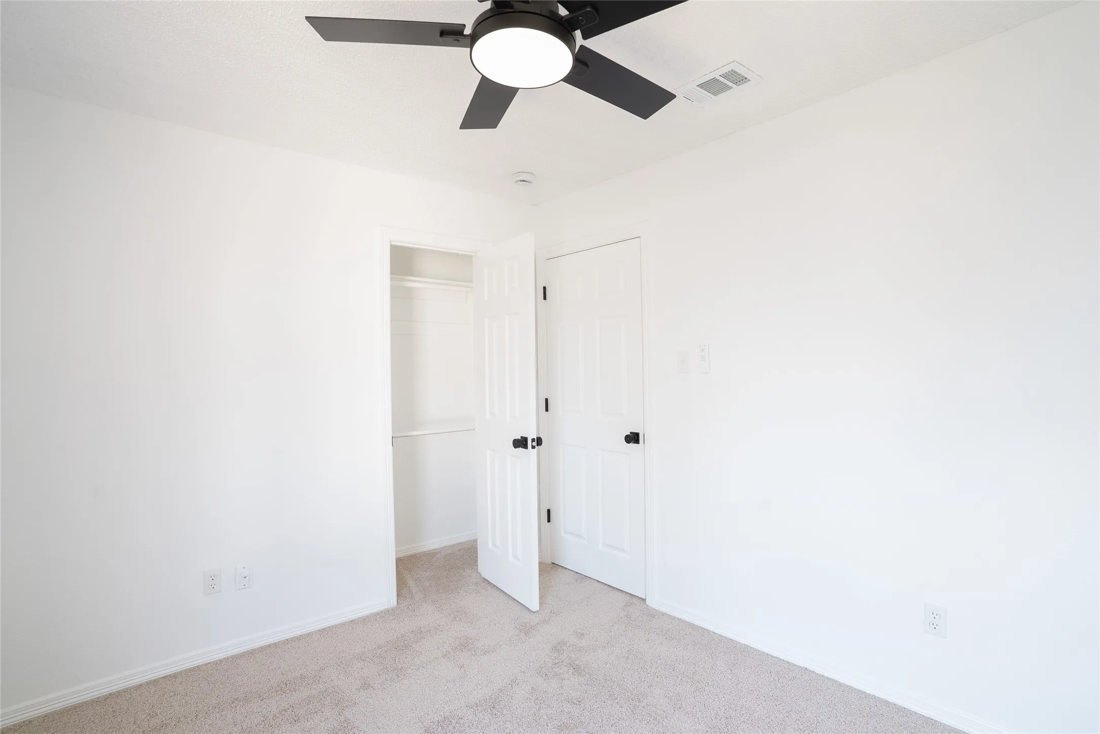 Plush carpet flooring, white painted walls, ceiling fan with integrated lighting, built-in closet with shelving, and white panel doors