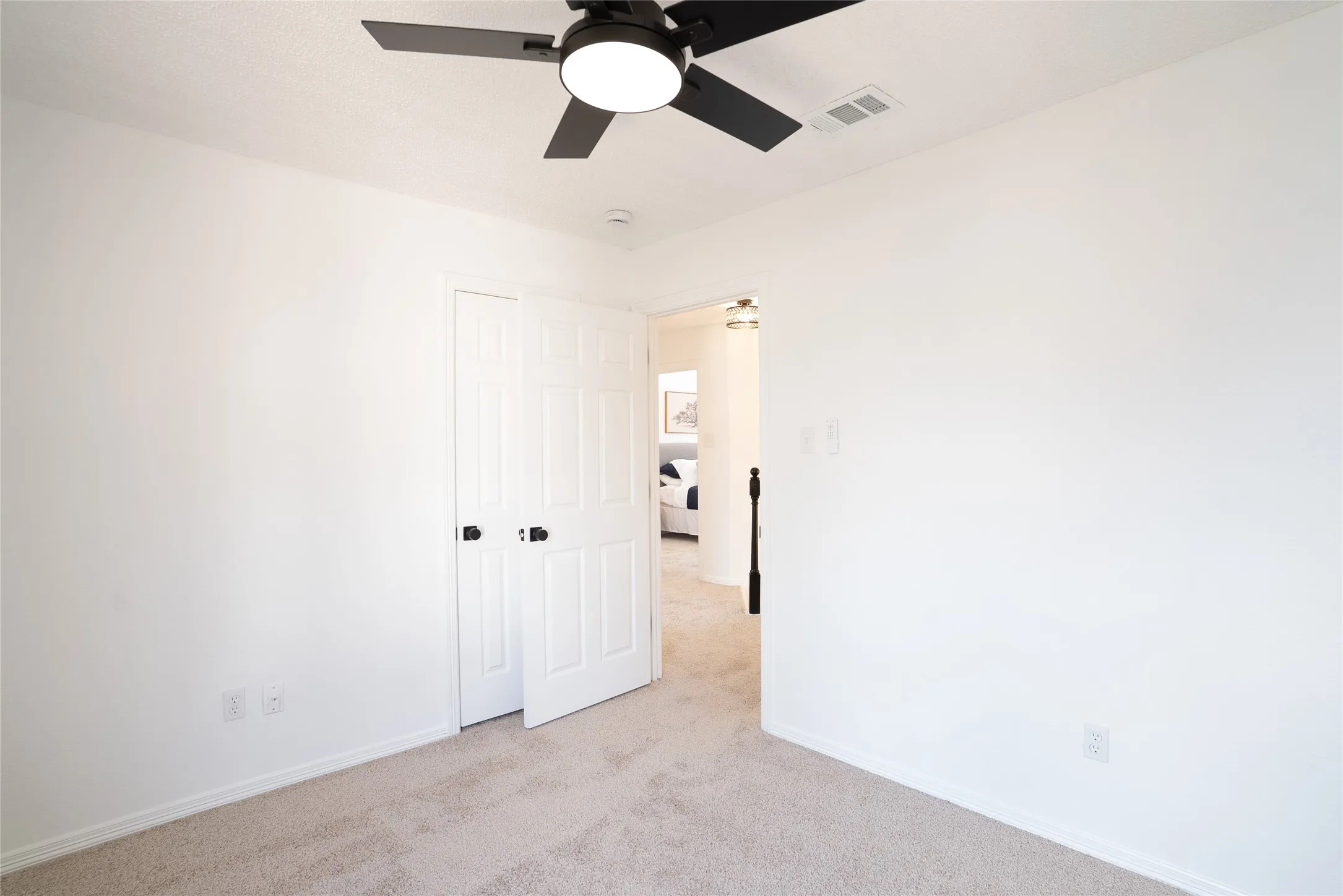 Carpeted room with white walls, a ceiling fan with integrated lighting, and a white paneled door