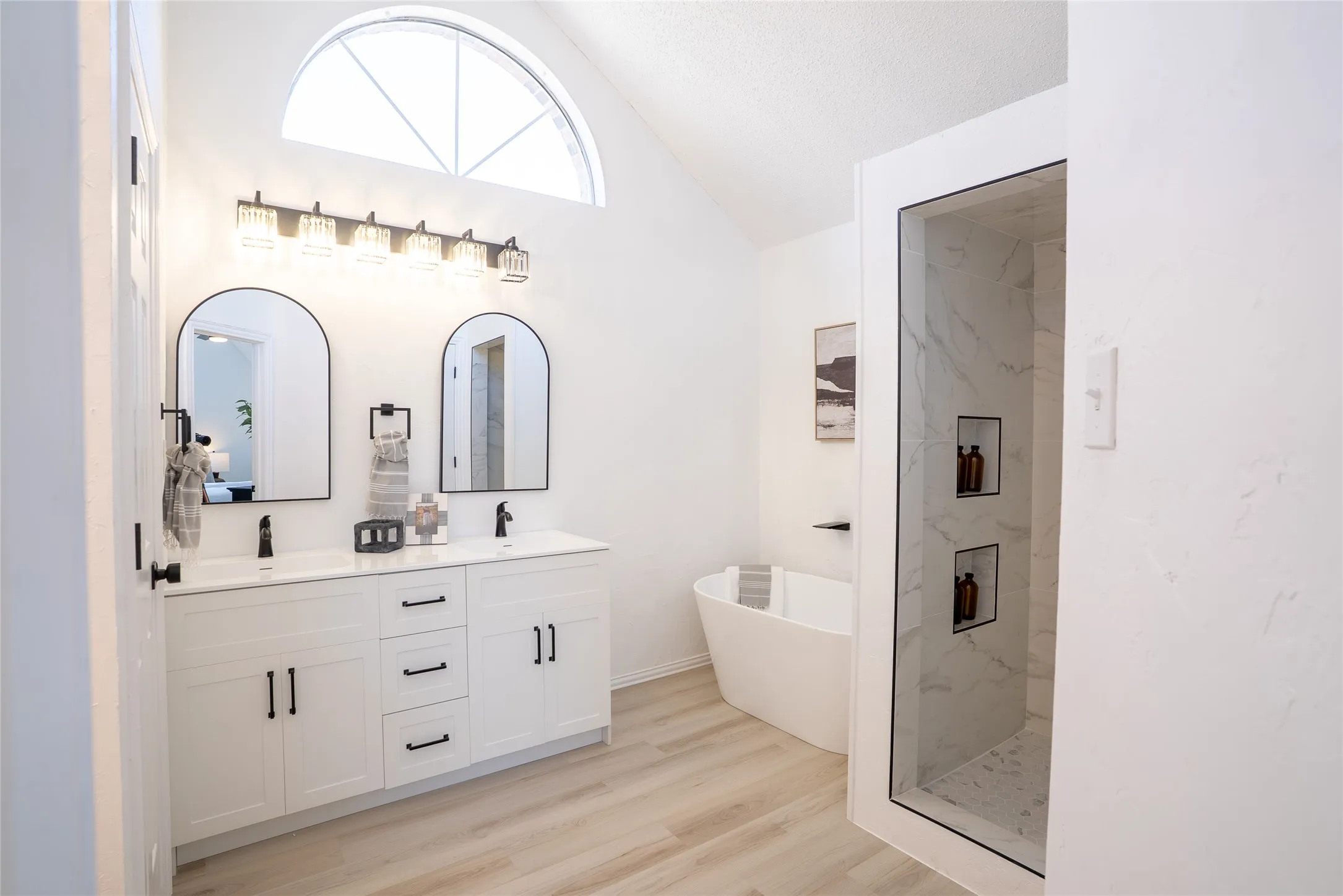 Bathroom featuring a double vanity with matte black hardware, arched mirrors, a freestanding soaking tub, and a walk-in shower with built-in shelving