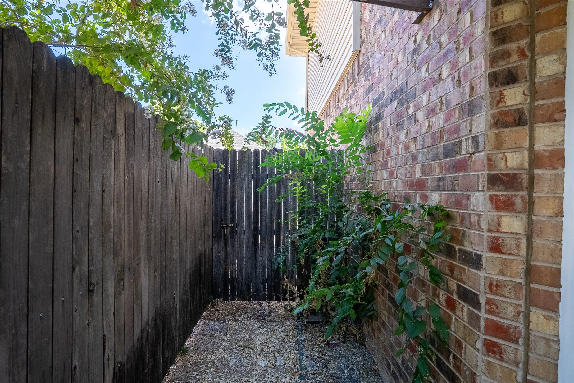 Brick exterior wall, wood fence, wood gate, and gravel ground cover
