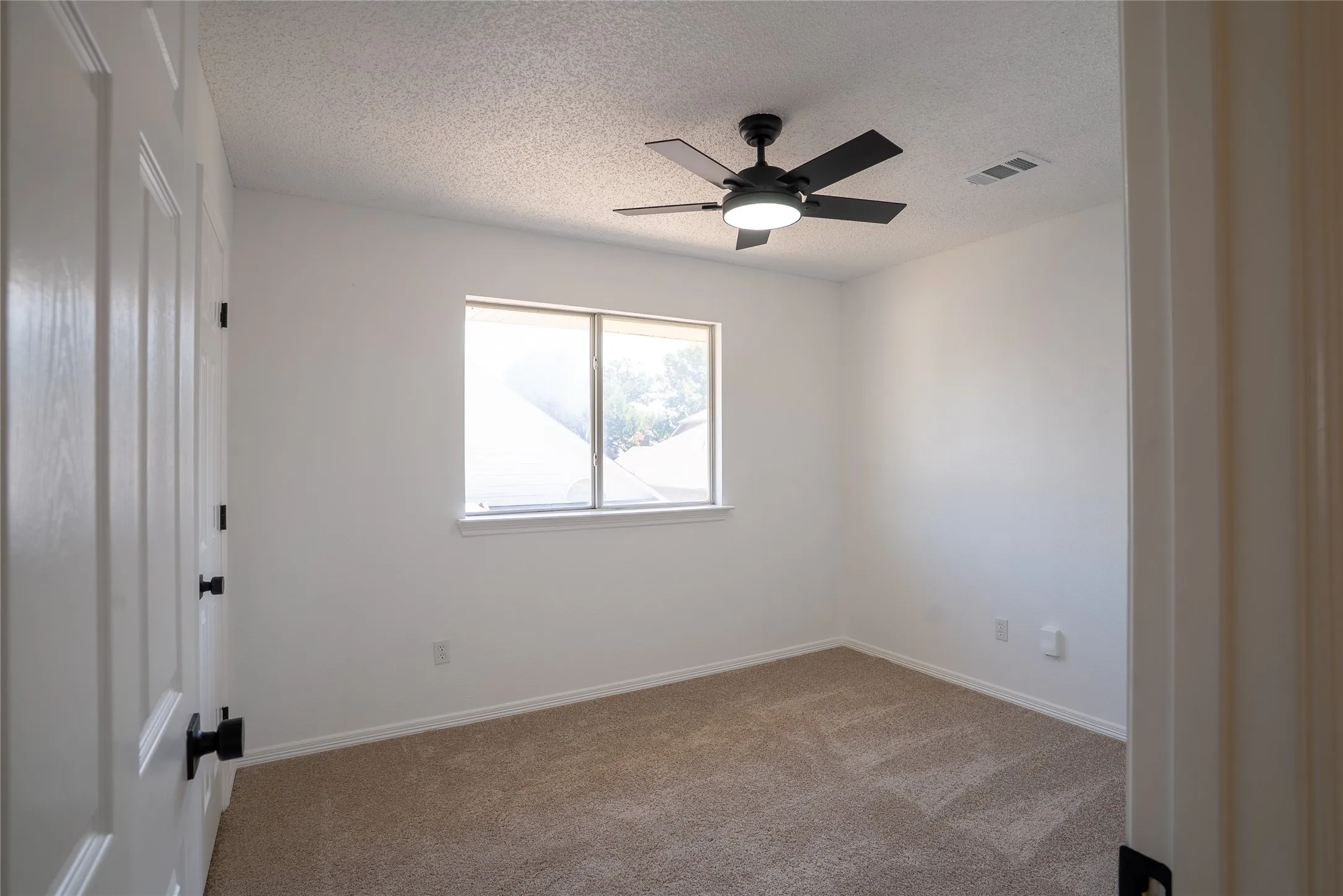 Recessed window with natural light, neutral carpet flooring, modern ceiling fan with integrated lighting, and white paneled door with matte black hardware