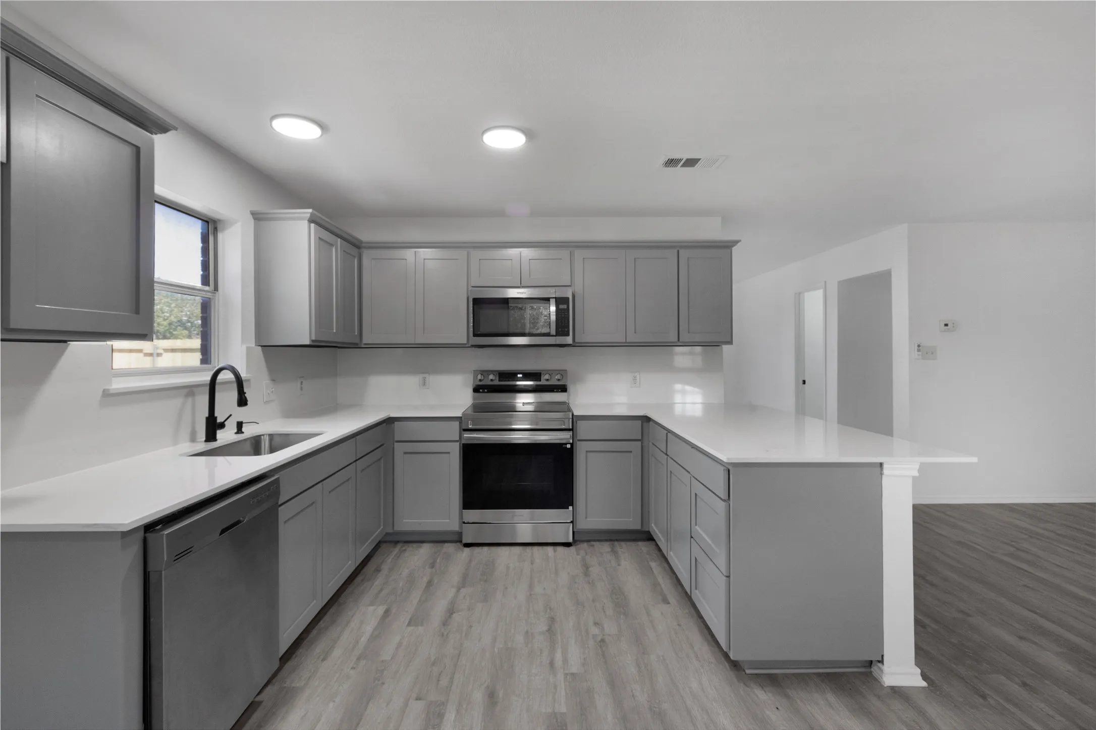 U-shaped kitchen featuring grey cabinetry, white countertops, stainless steel appliances, and wood-finish flooring