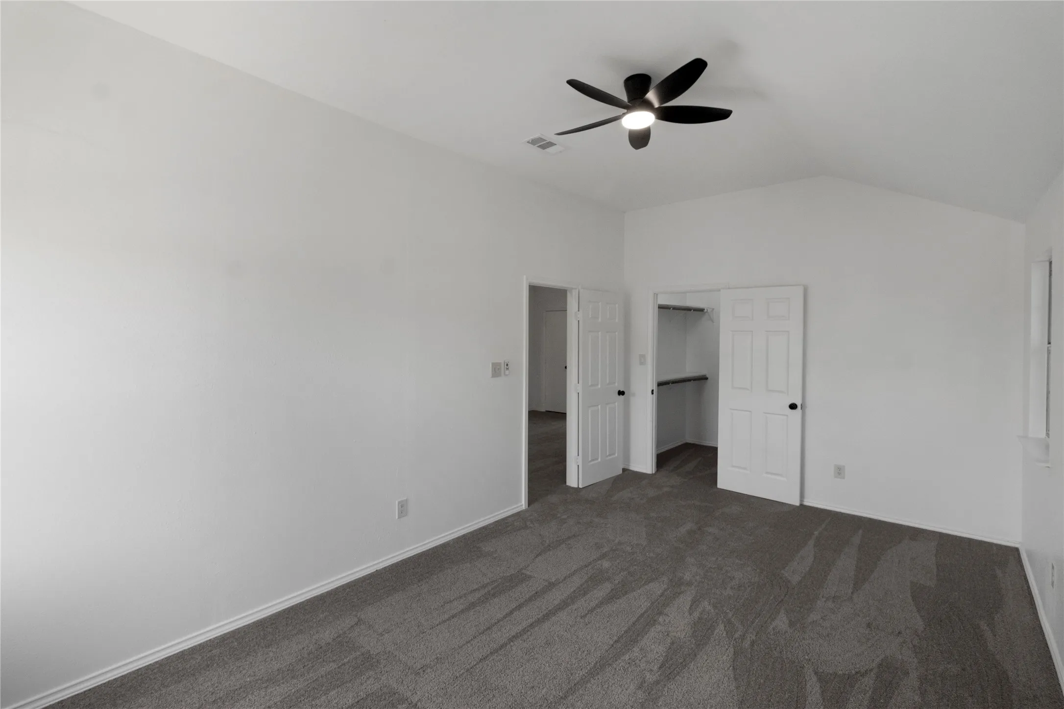Vaulted ceiling with a ceiling fan, plush carpet flooring, and a walk-in closet with shelving