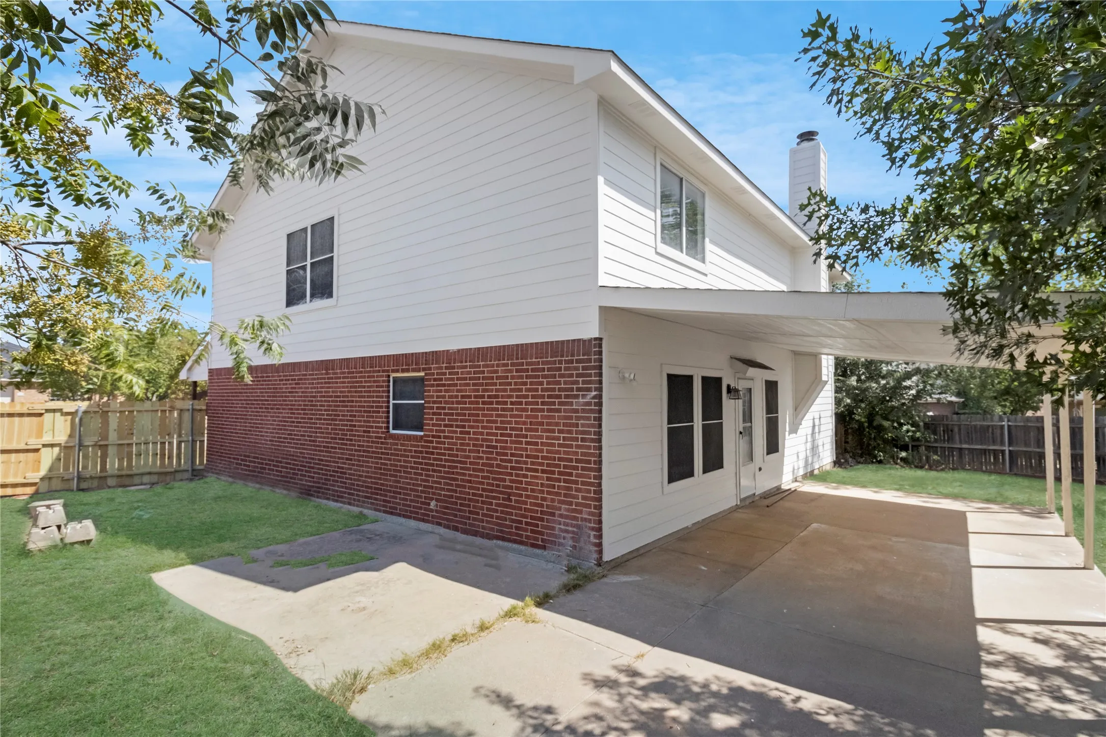 Two-story exterior with a brick and white siding facade, featuring a patio area with a covered extension, and a wood privacy fence