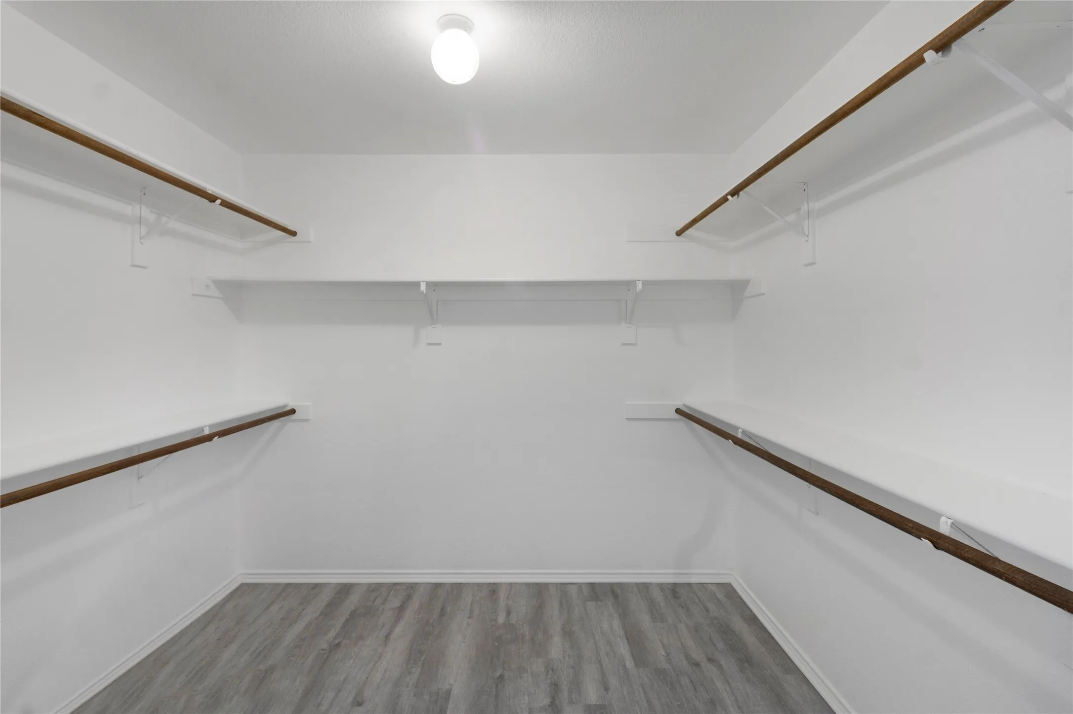 Walk-in closet featuring wood-finish flooring, white walls, and built-in shelving with hanging rods