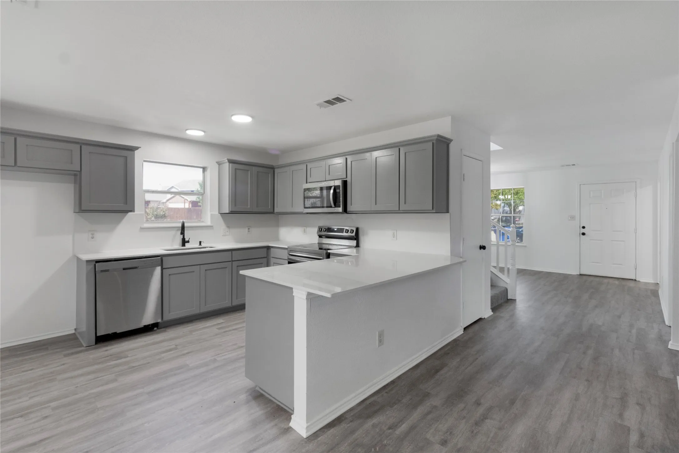 Kitchen featuring gray cabinetry, white countertops, stainless steel appliances, and wood-finish flooring