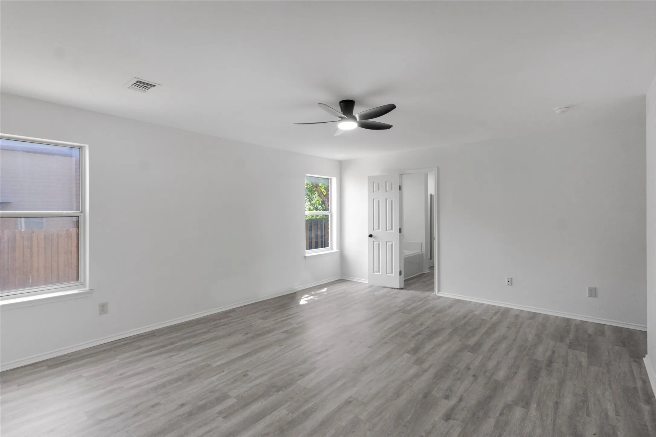Spacious interior with neutral white walls, wood-finish flooring, multiple windows, and a ceiling fan