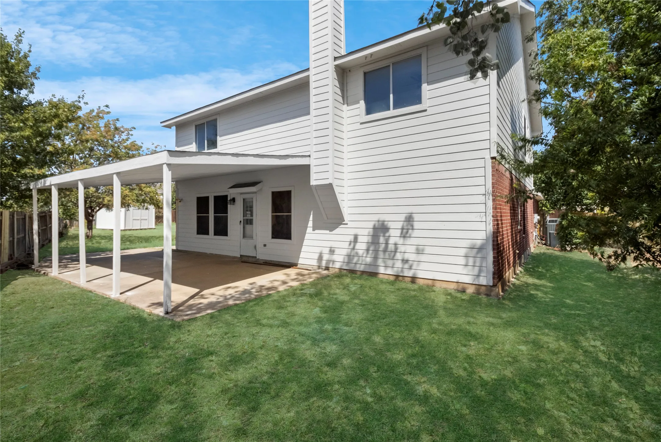 Exterior featuring white siding, a covered patio with a concrete slab, a brick foundation, and a lush green lawn