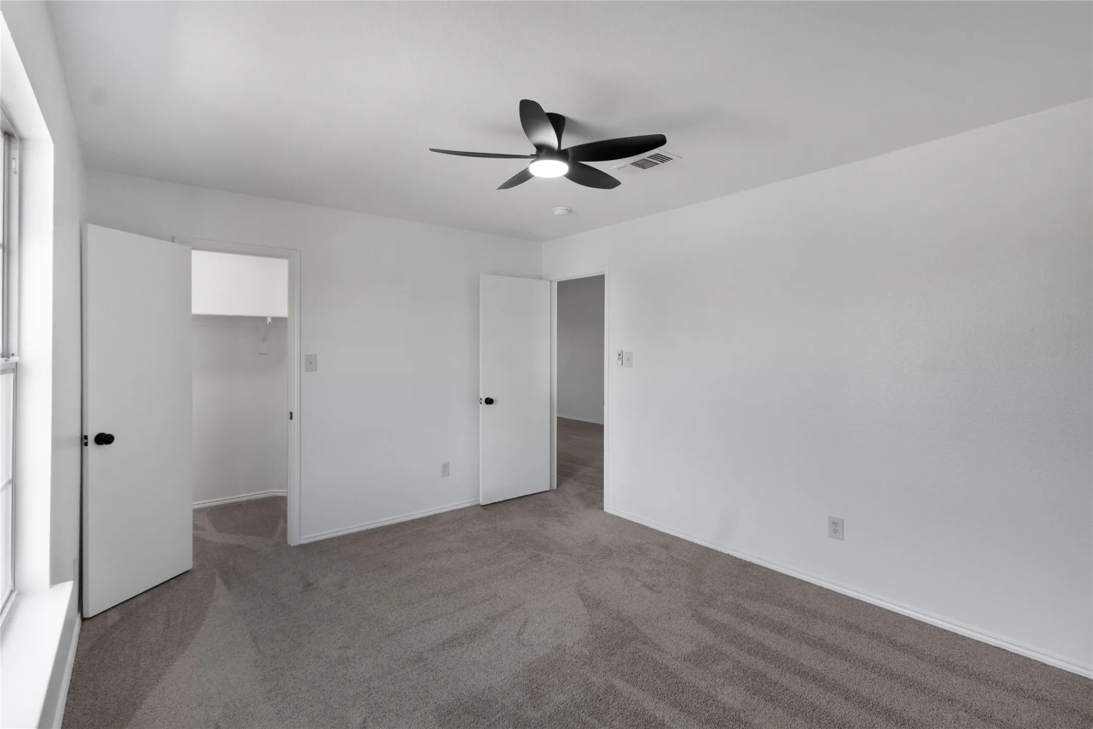 Neutral toned carpeting, white walls, black ceiling fan, white trim, and white doors