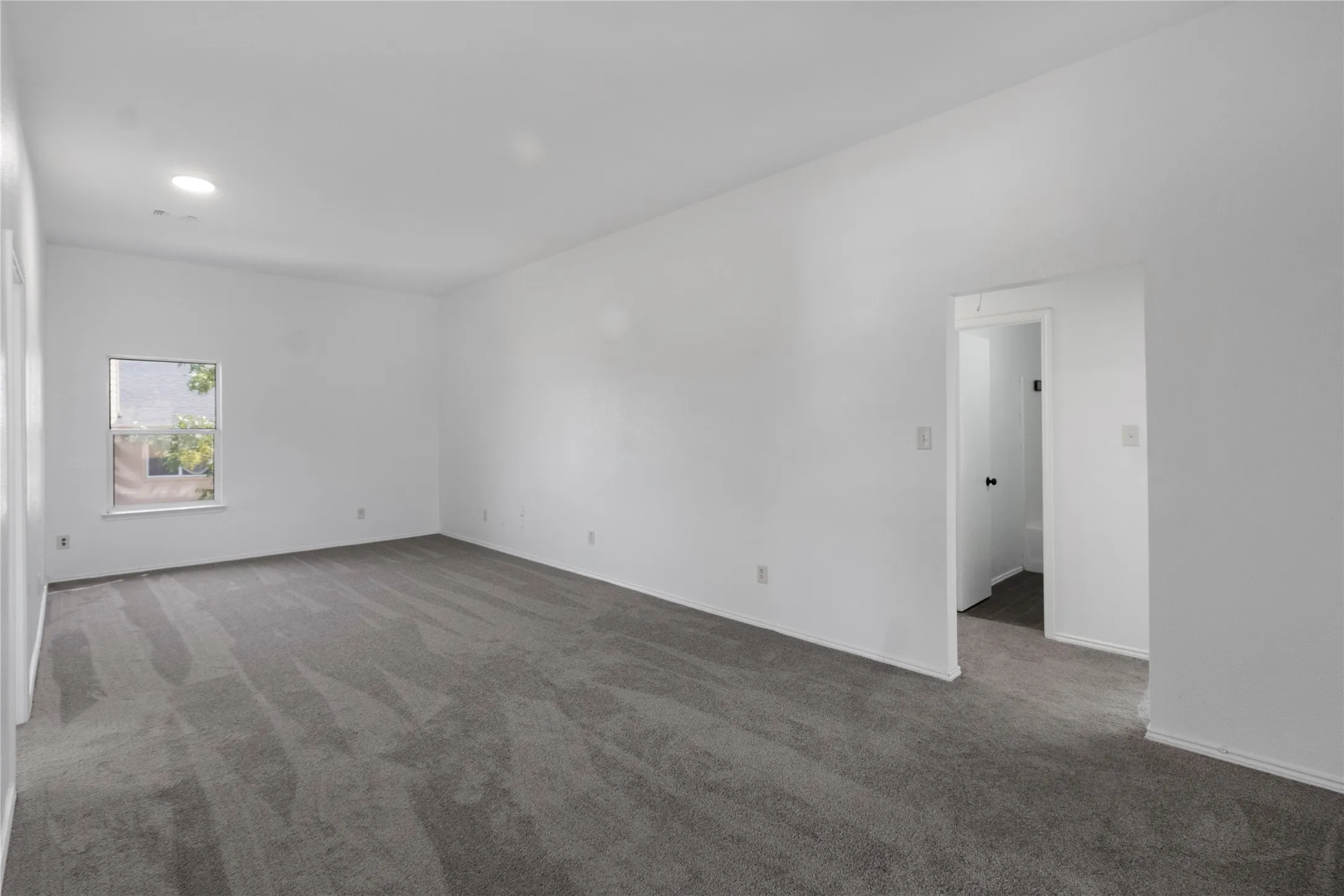 Spacious room featuring neutral carpeting, white walls, a recessed ceiling light, and a window for ambient light