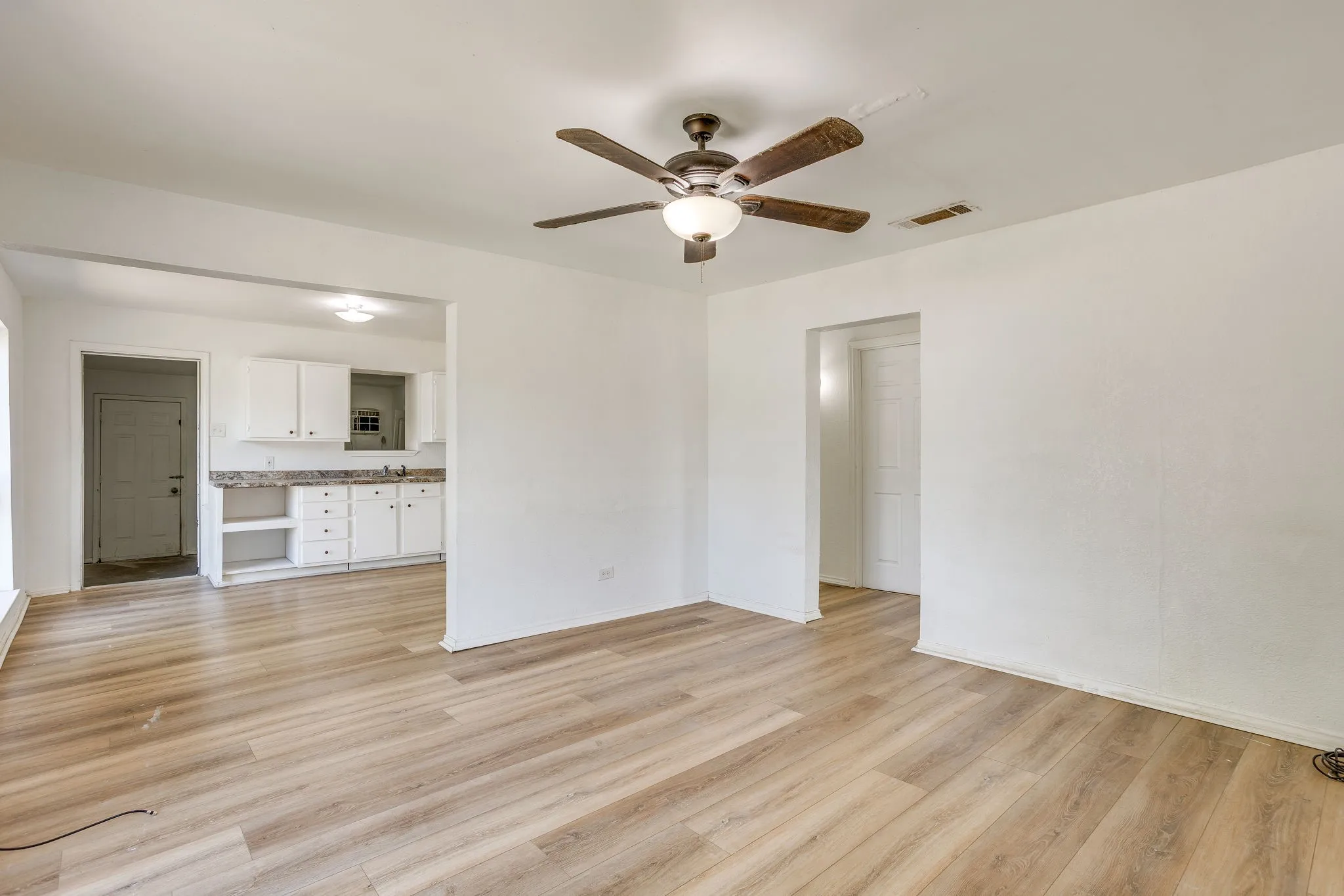 Living room open to the kitchen with laminate wood-like flooring and neutral paint light and bright.