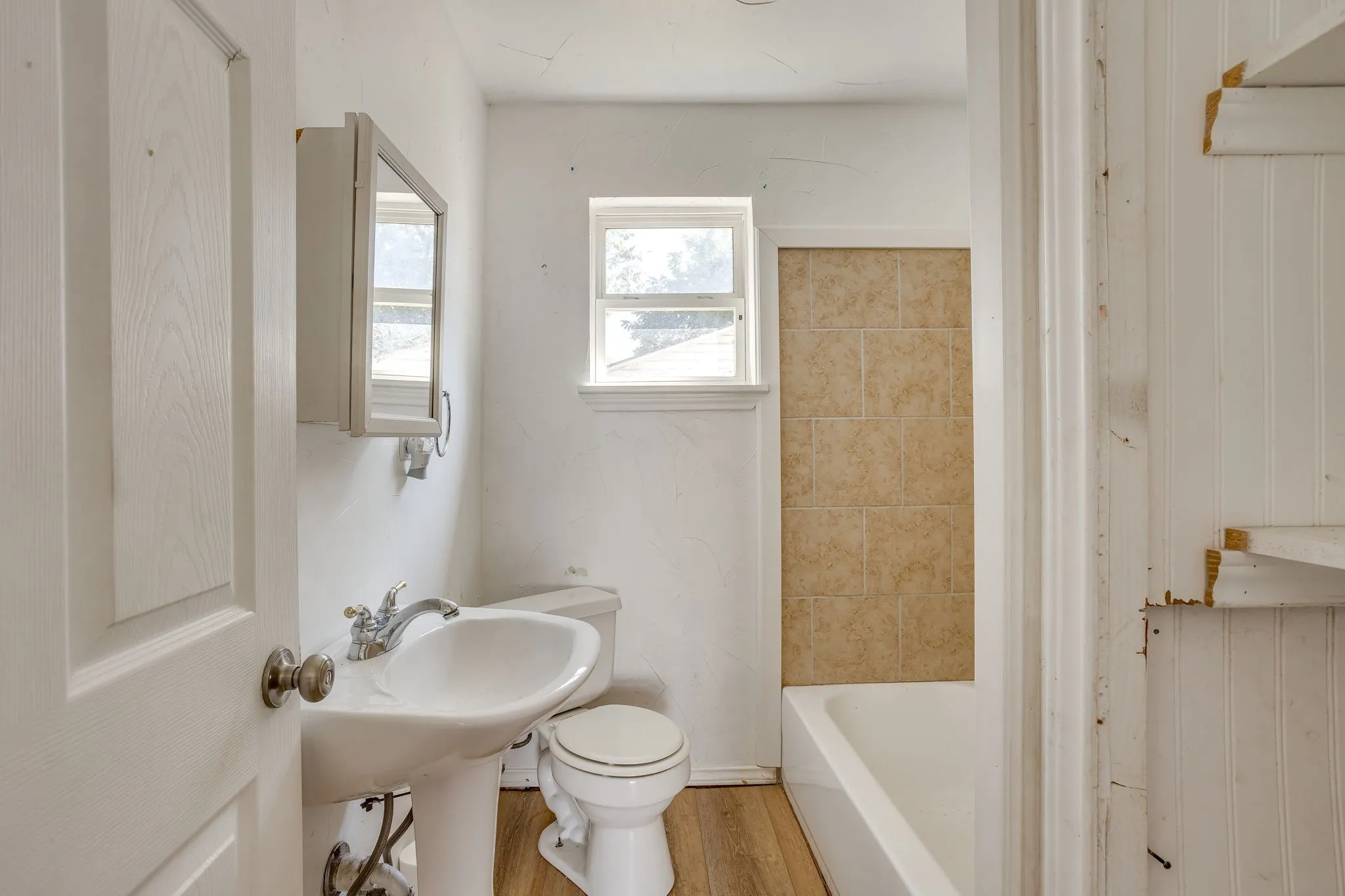 Hallway bath with pedestal sink, linen closet, laminate flooring, medicine cabinet and tiled shower and tub.
