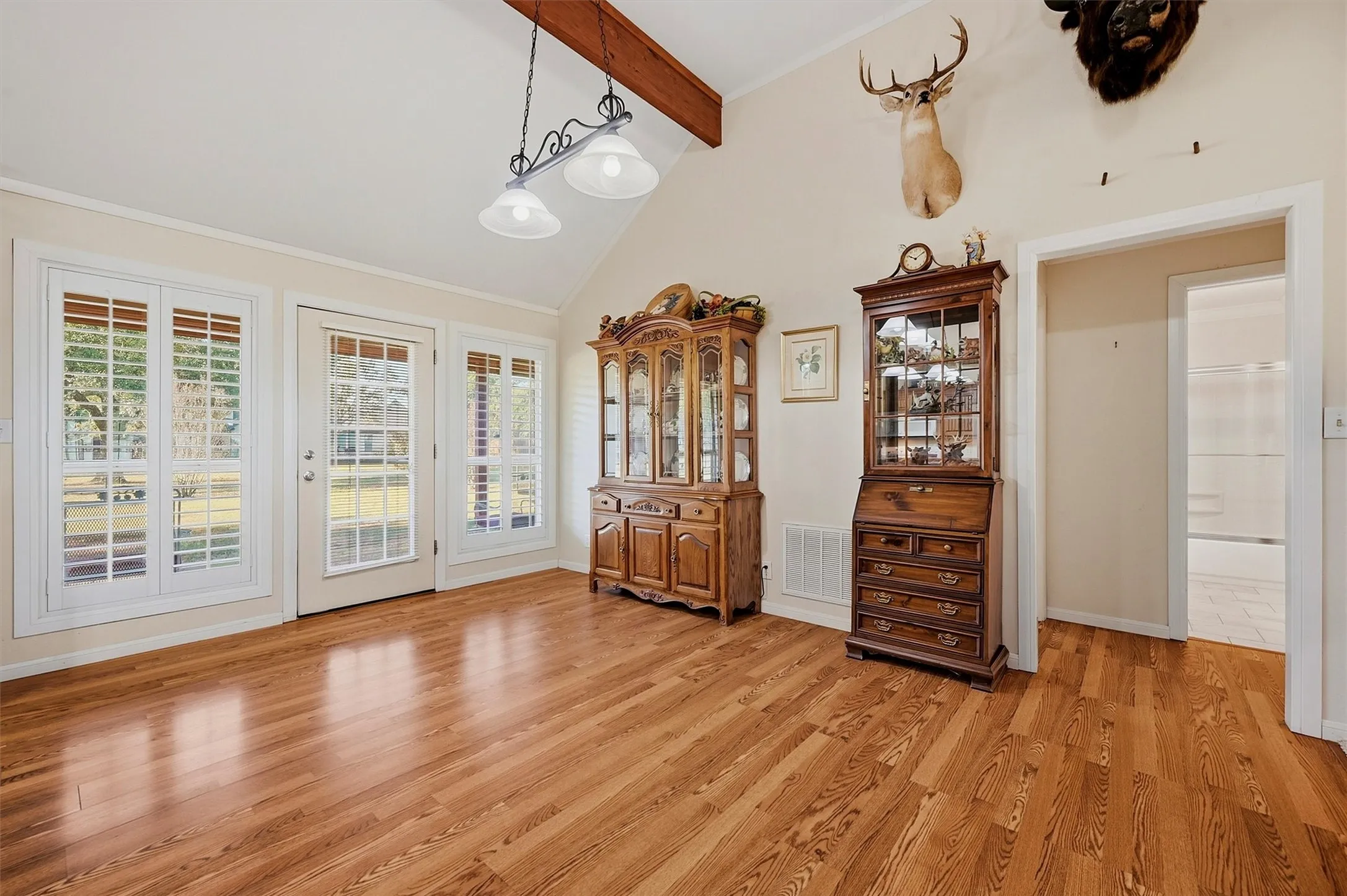 Vaulted ceiling with exposed wood beam, wood-finish flooring, white plantation shutters, and a transom door with side windows