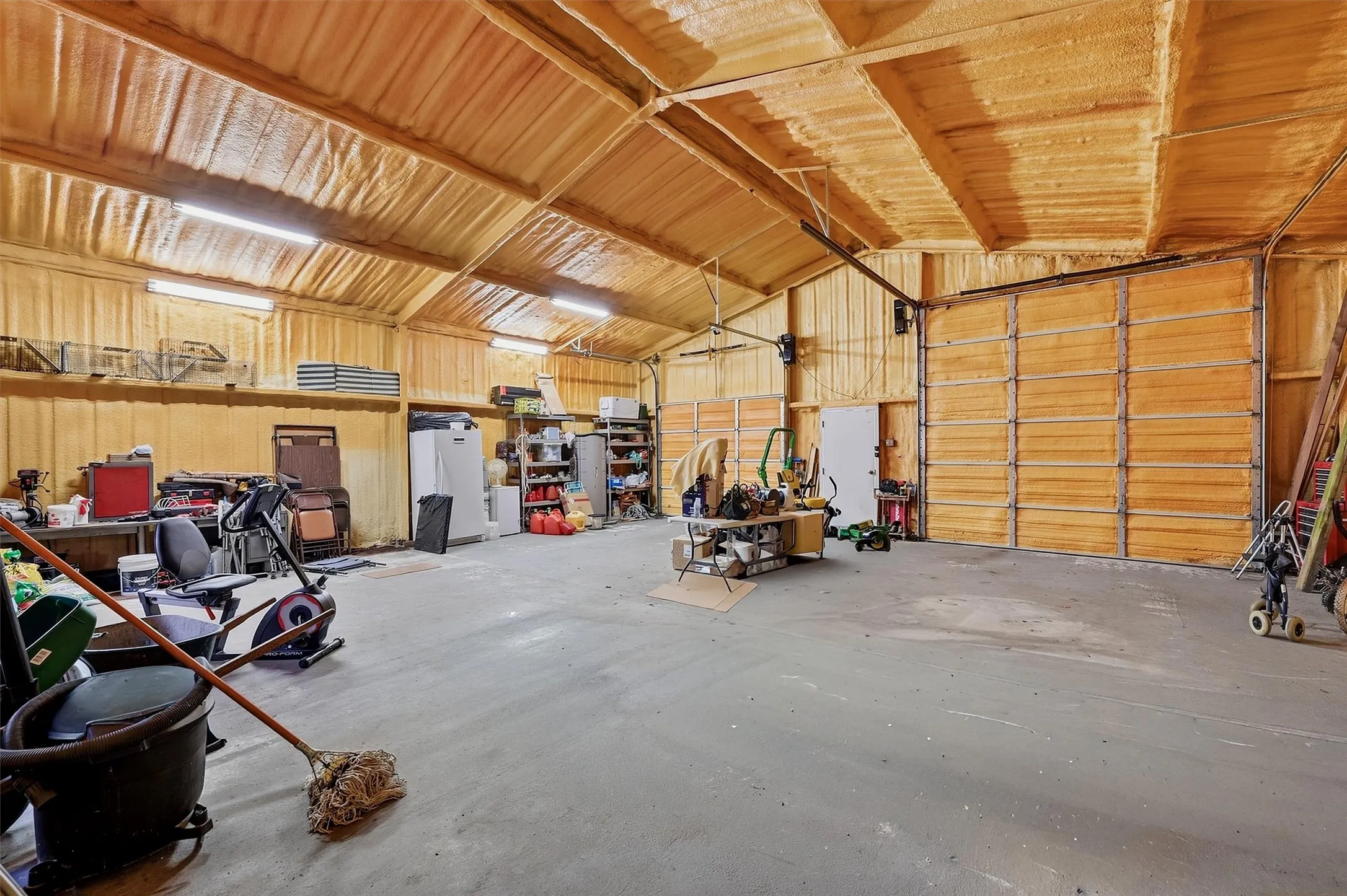 Spacious garage with exposed beam ceiling, concrete flooring, dual overhead doors, and fluorescent lighting