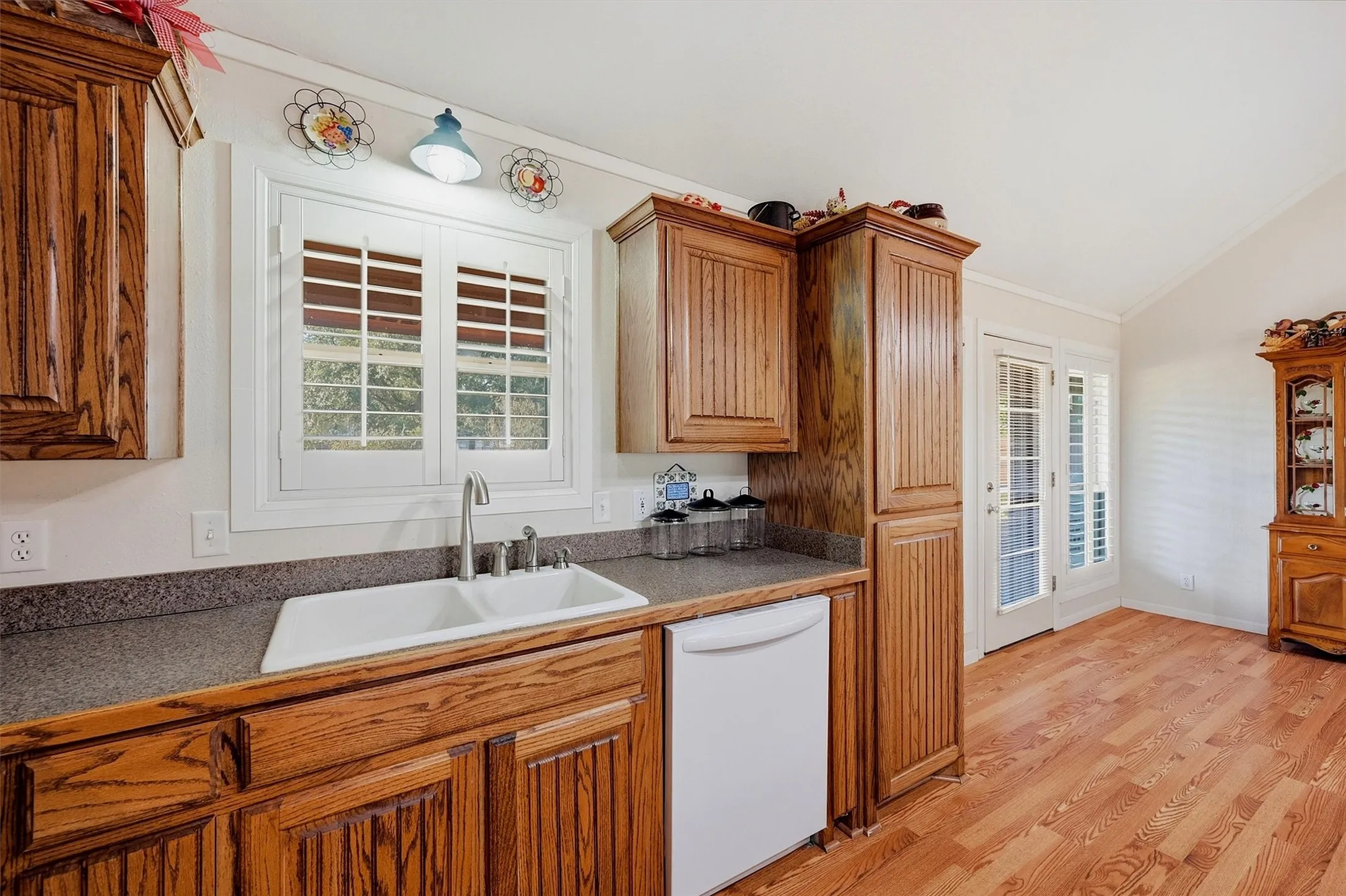 Wood-finish cabinetry, solid surface countertops, double basin sink, and wood-finish flooring