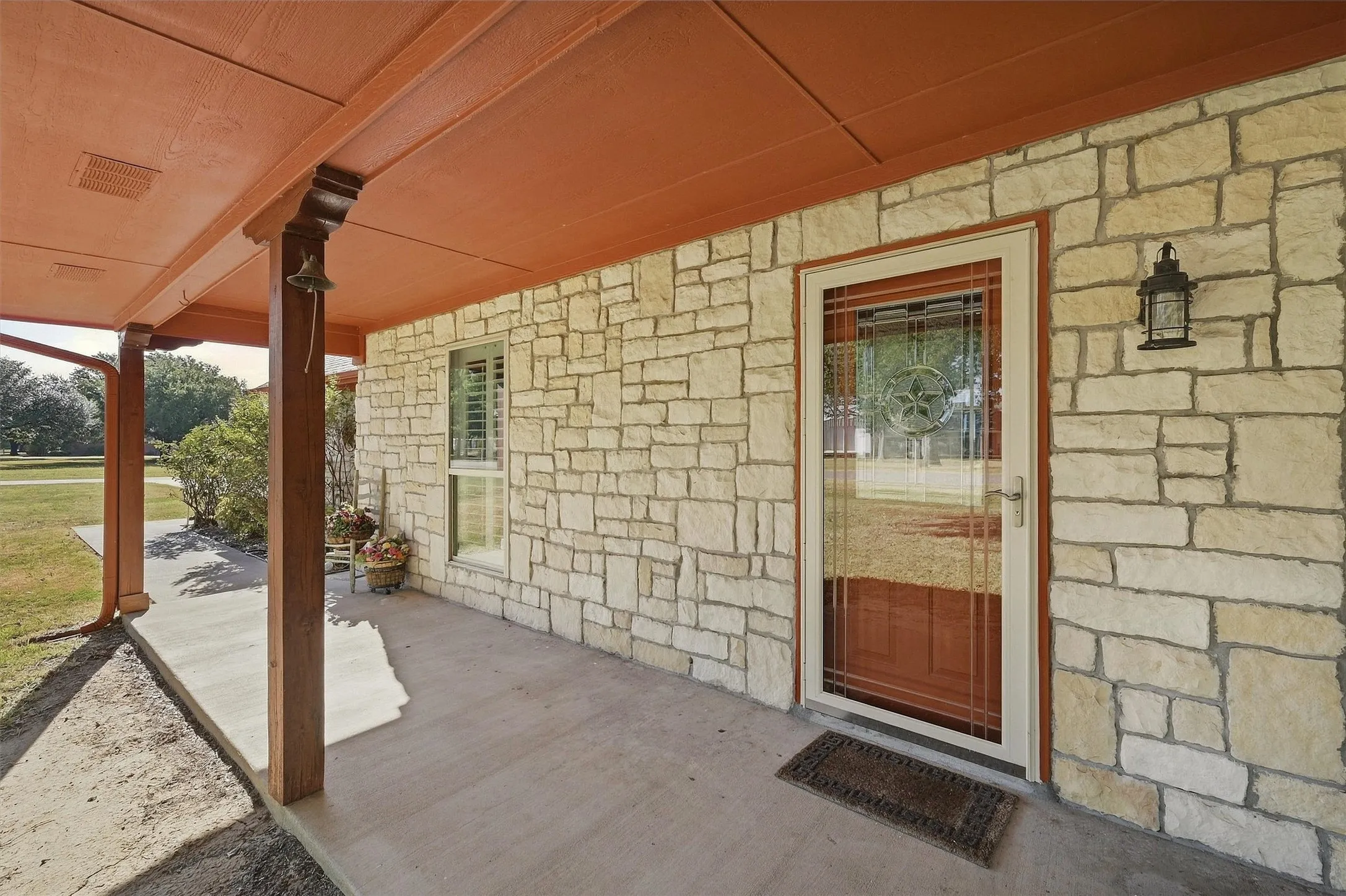 Stone-clad exterior featuring a covered front porch with stained wood columns, an entryway with a storm door, and a wall-mounted exterior light fixture