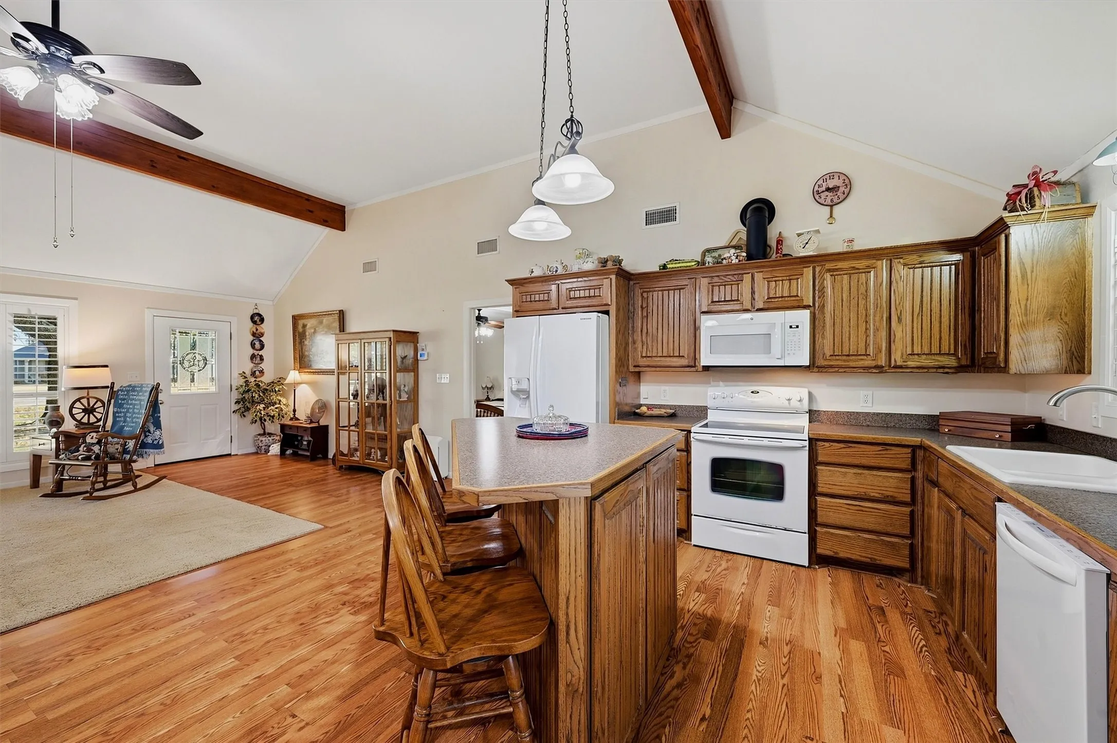 Vaulted ceiling with exposed wood beams, wood-finish flooring, recessed lighting, and a kitchen island with seating