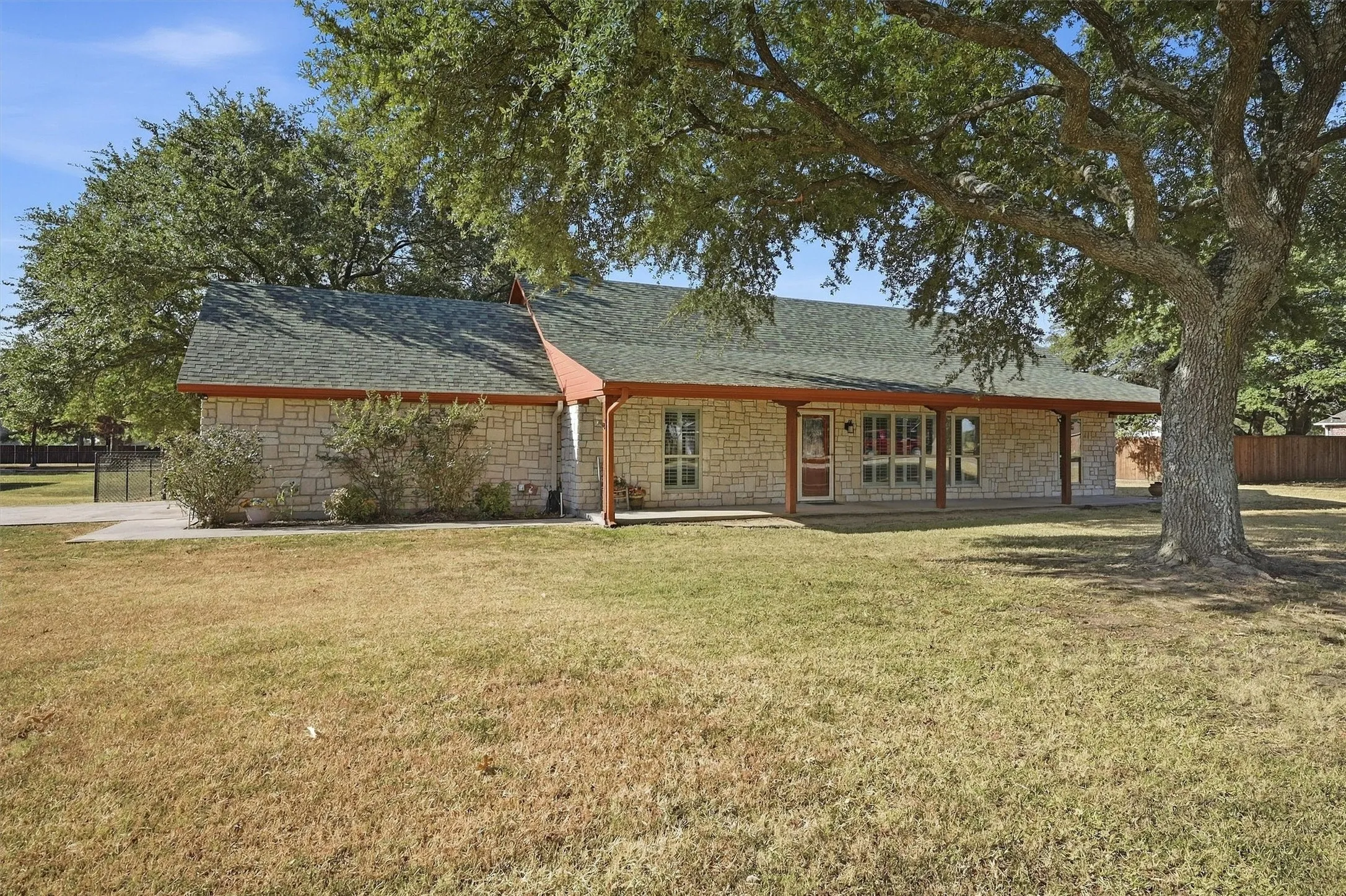 Stone facade residence with a covered front porch, asphalt shingle roof, and mature trees