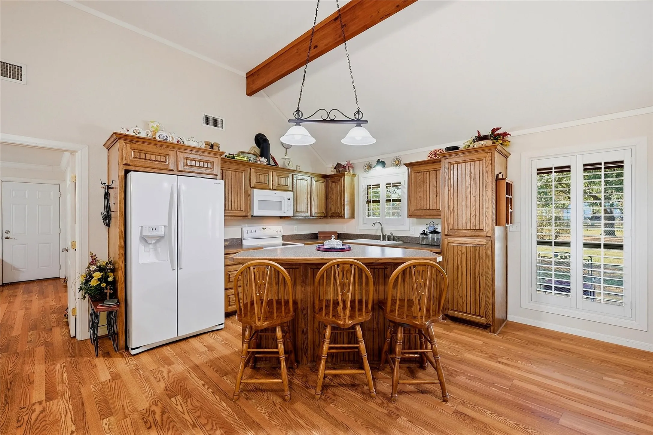 Kitchen featuring a vaulted ceiling with exposed wood beam, wood-finish flooring, wood cabinetry, a central island, and white appliances