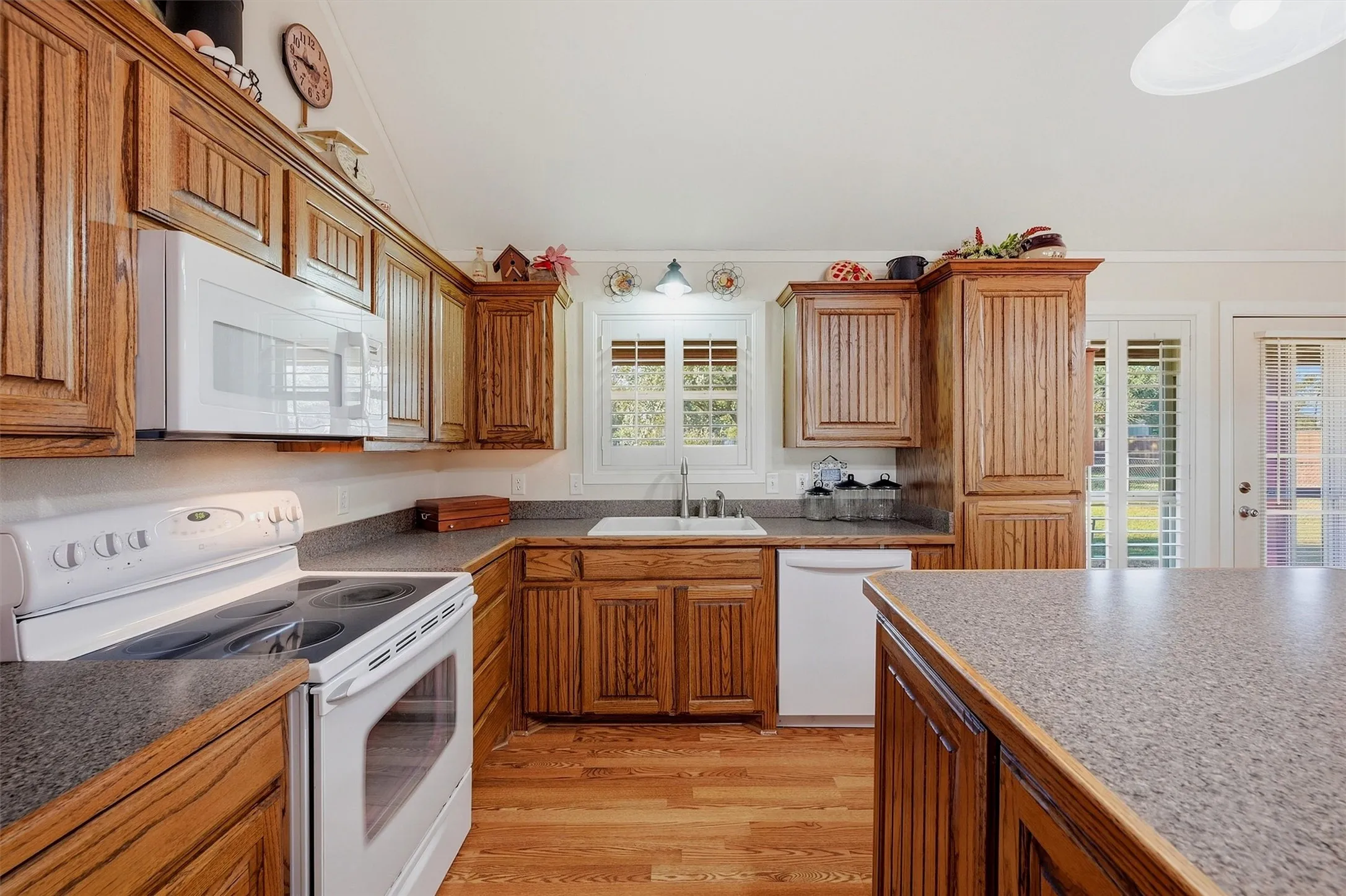 Kitchen featuring wood-finish cabinetry, solid surface countertops, a white built-in microwave, white electric range, and wood-finish flooring