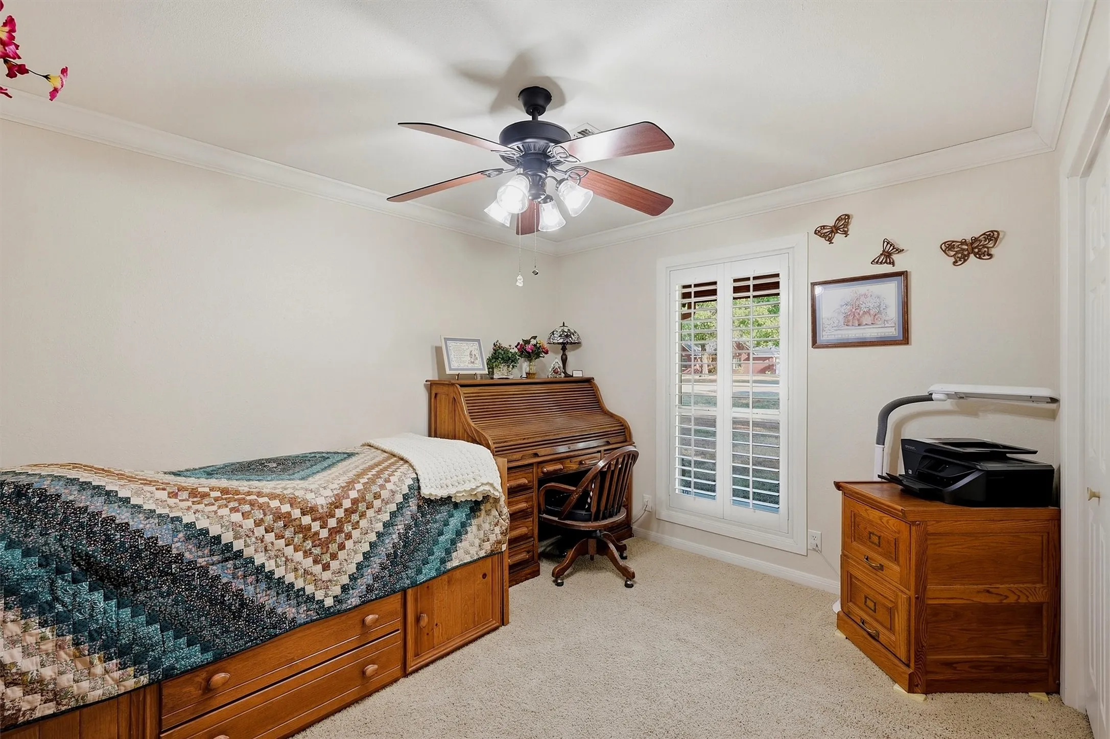 Crown molding, carpeted flooring, window with plantation shutters, ceiling fan with light fixture