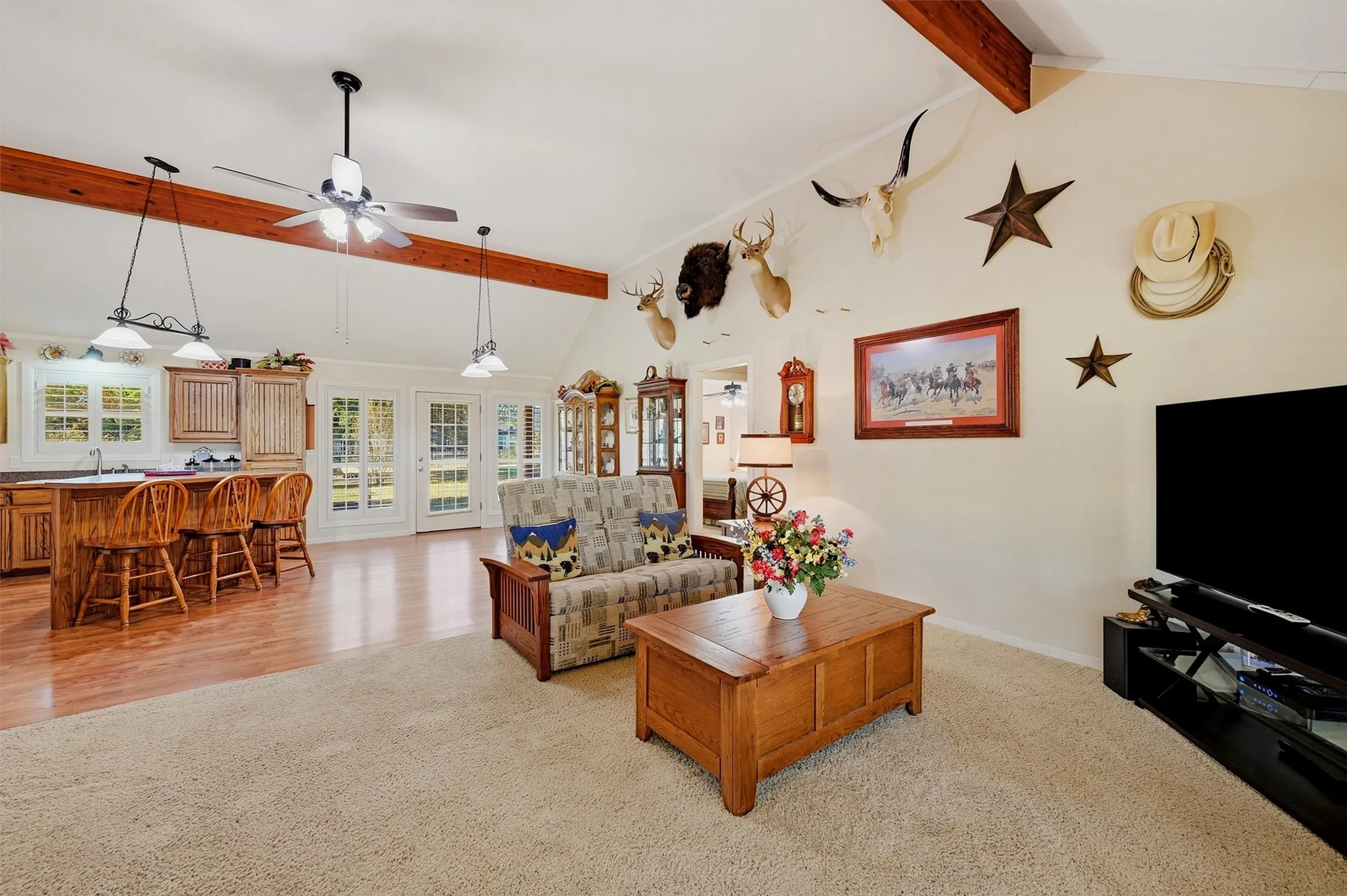 Vaulted ceiling with exposed wood beams, wood-finish flooring, white double French doors, kitchen island with seating, and a ceiling fan with integrated lighting