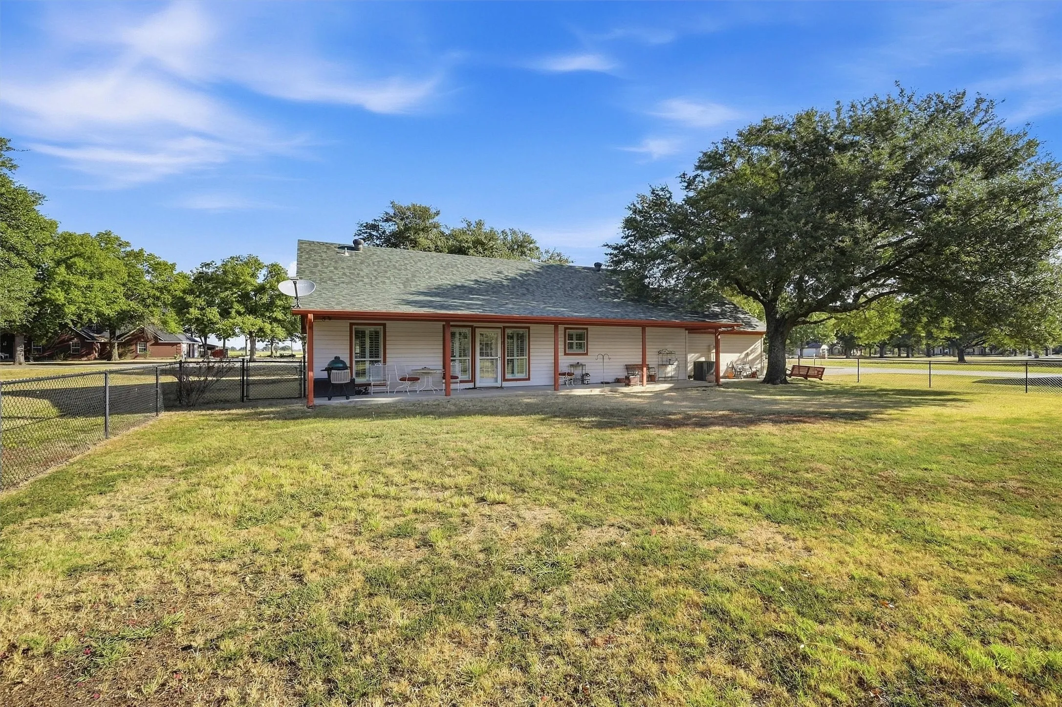 Expansive lawn with a mature shade tree, a covered patio, and a chain-link fence