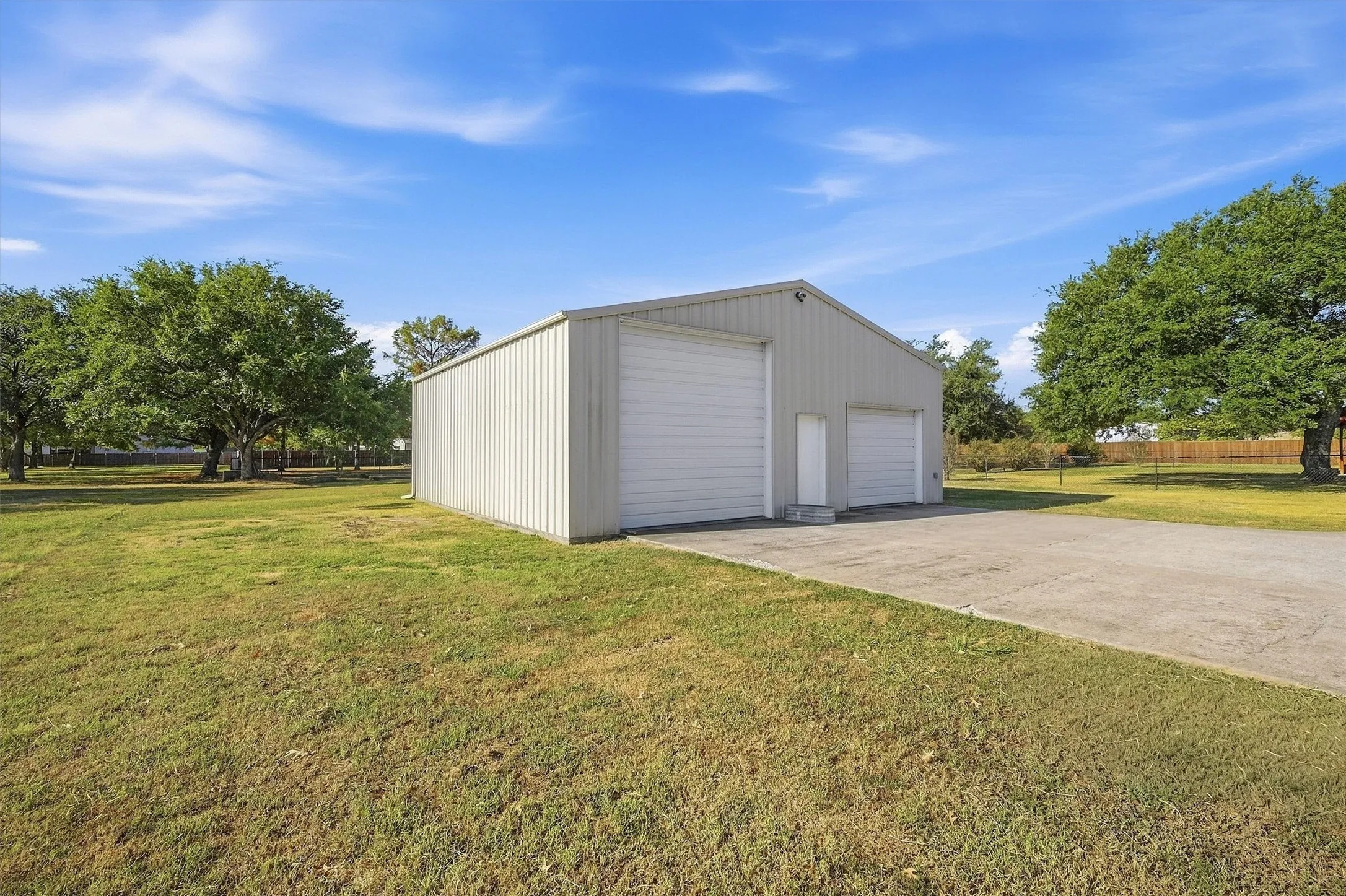 Metal-sided utility building with two roll-up garage doors, an exterior side door, and a concrete approach