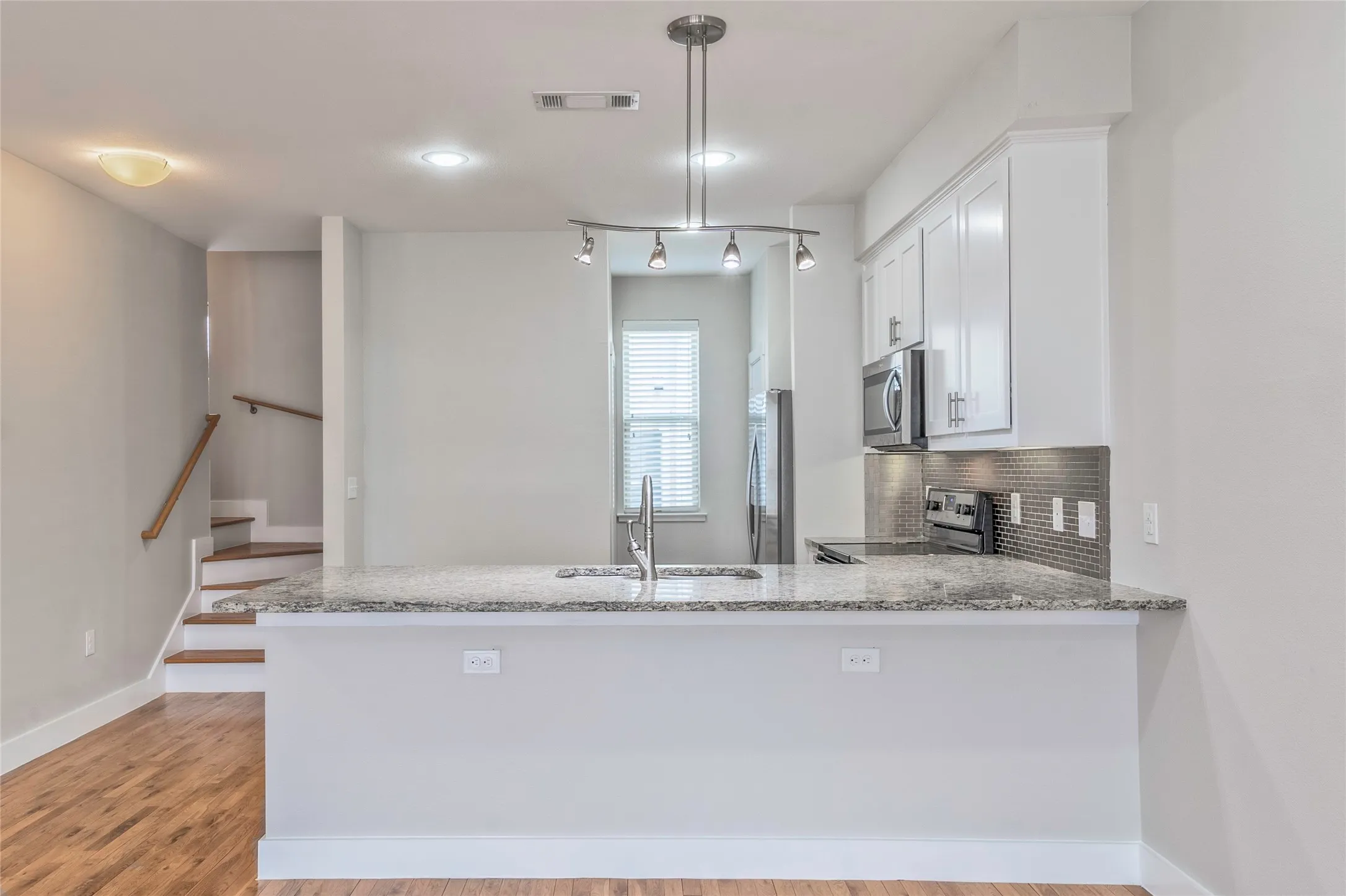 Kitchen island with granite countertop, integrated sink, and track lighting