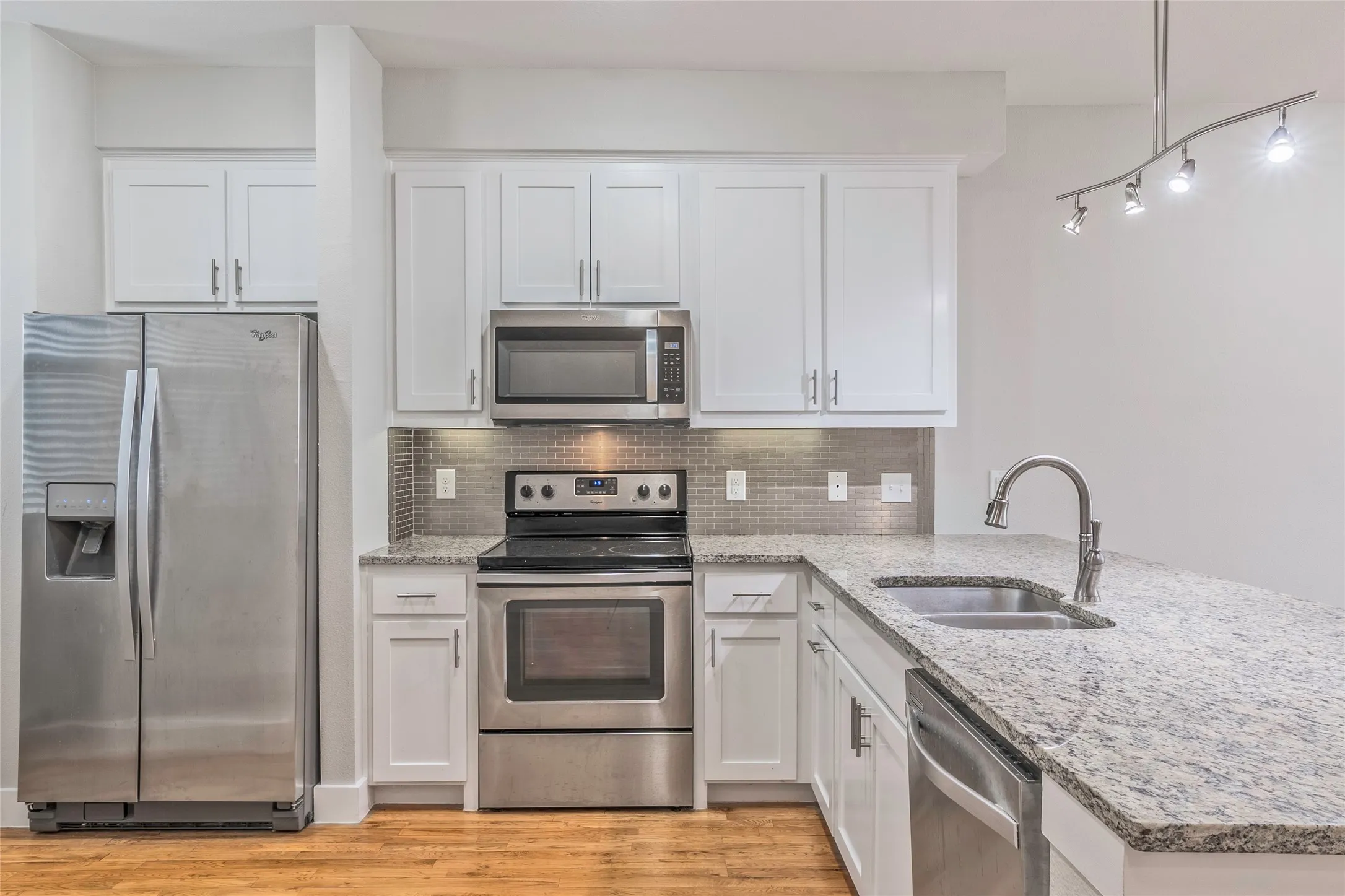 Kitchen featuring white cabinetry, stainless steel appliances, granite countertops, a tile backsplash, and wood-finish flooring