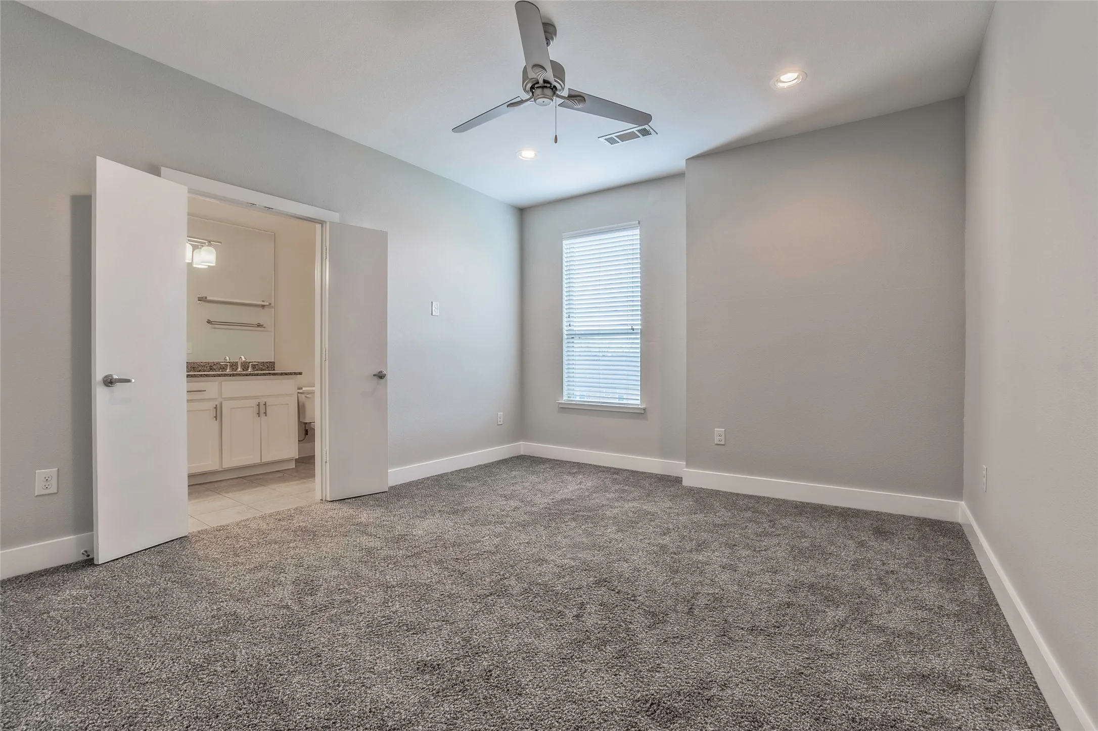 Gray carpeted room featuring a ceiling fan, recessed lighting, and a window with blinds