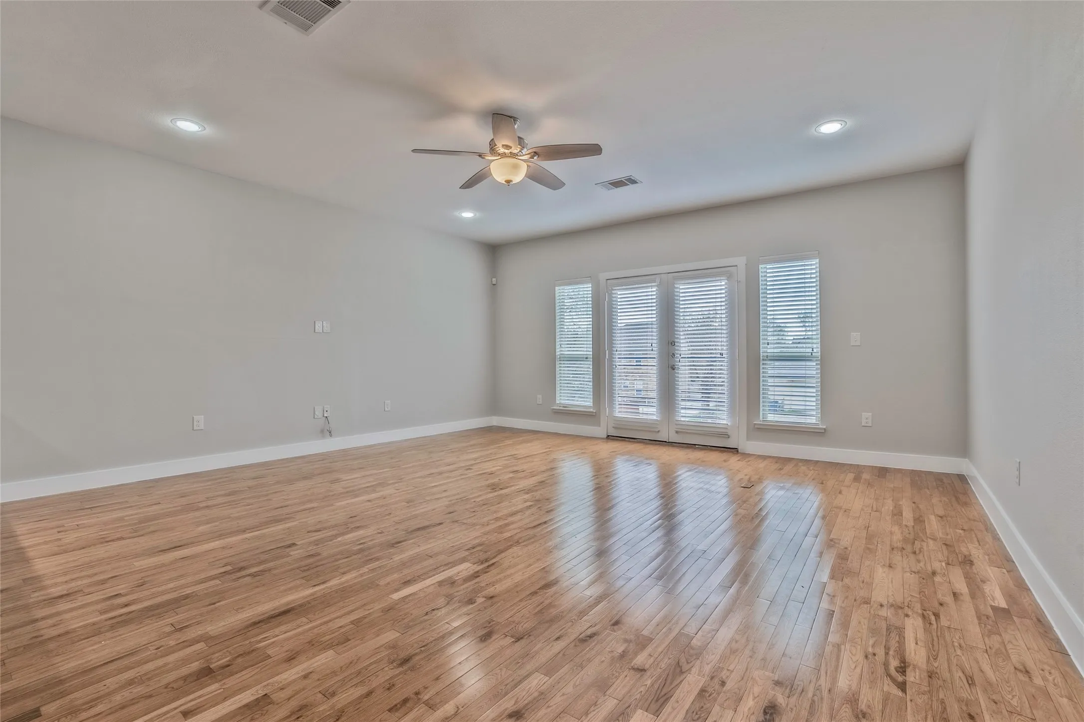 Spacious interior featuring wood-finish flooring, light gray walls, a ceiling fan, recessed lighting, and white French doors with side windows
