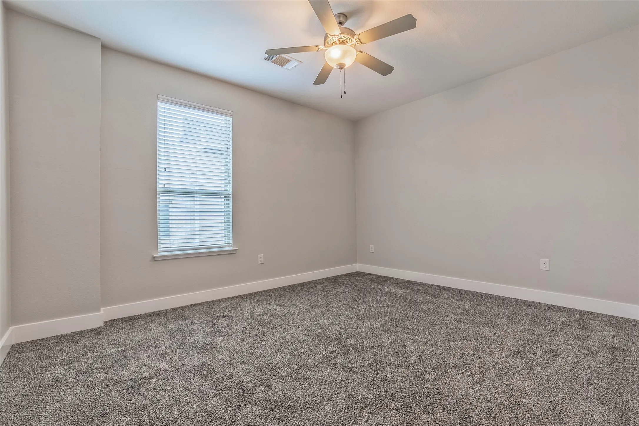 Neutral wall tones, grey carpeting, ceiling fan with integrated lighting, and a window with blinds