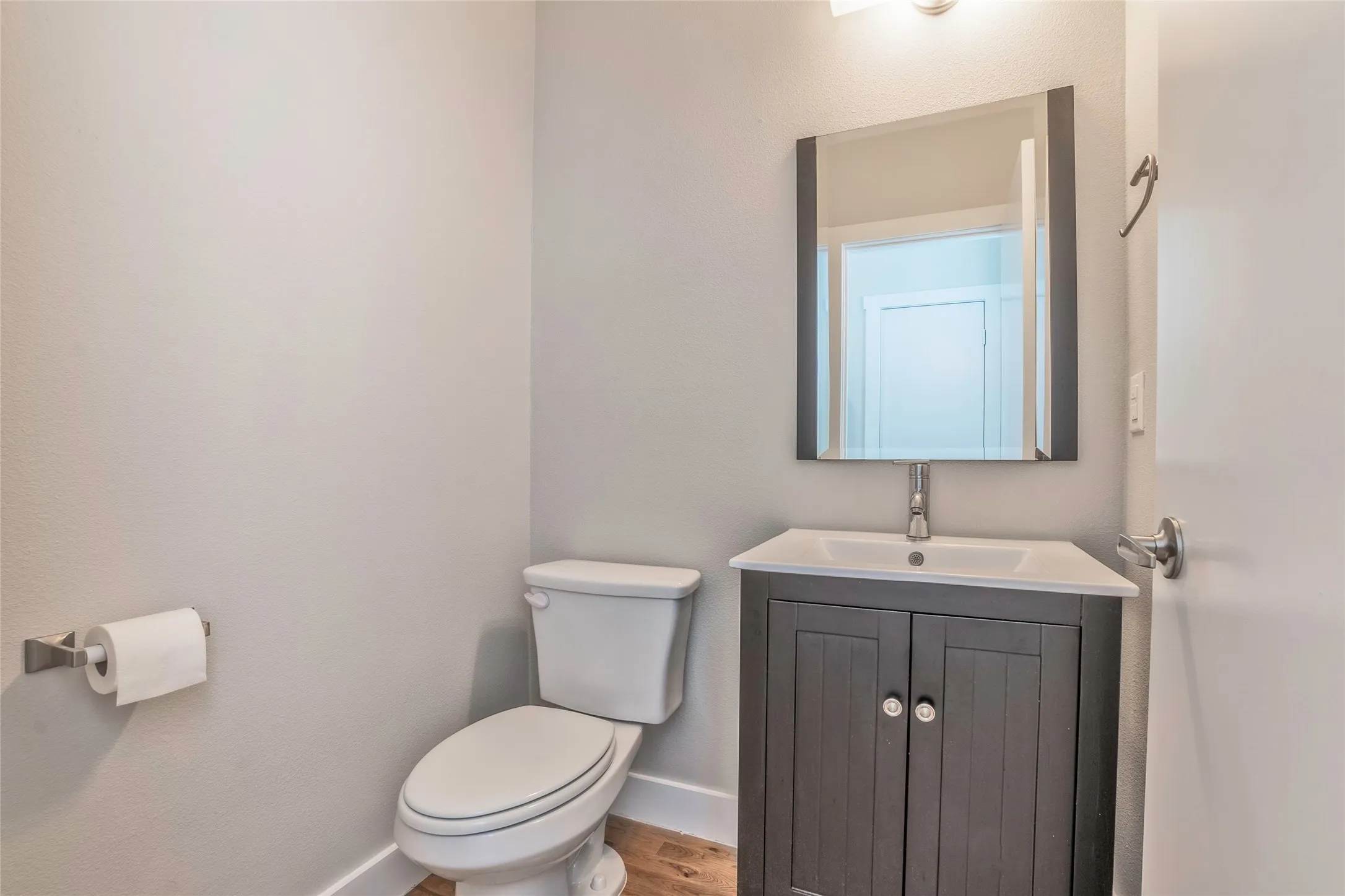 White toilet with a dark wood-finish vanity and white countertop, featuring a rectangular mirror and wall-mounted light fixture