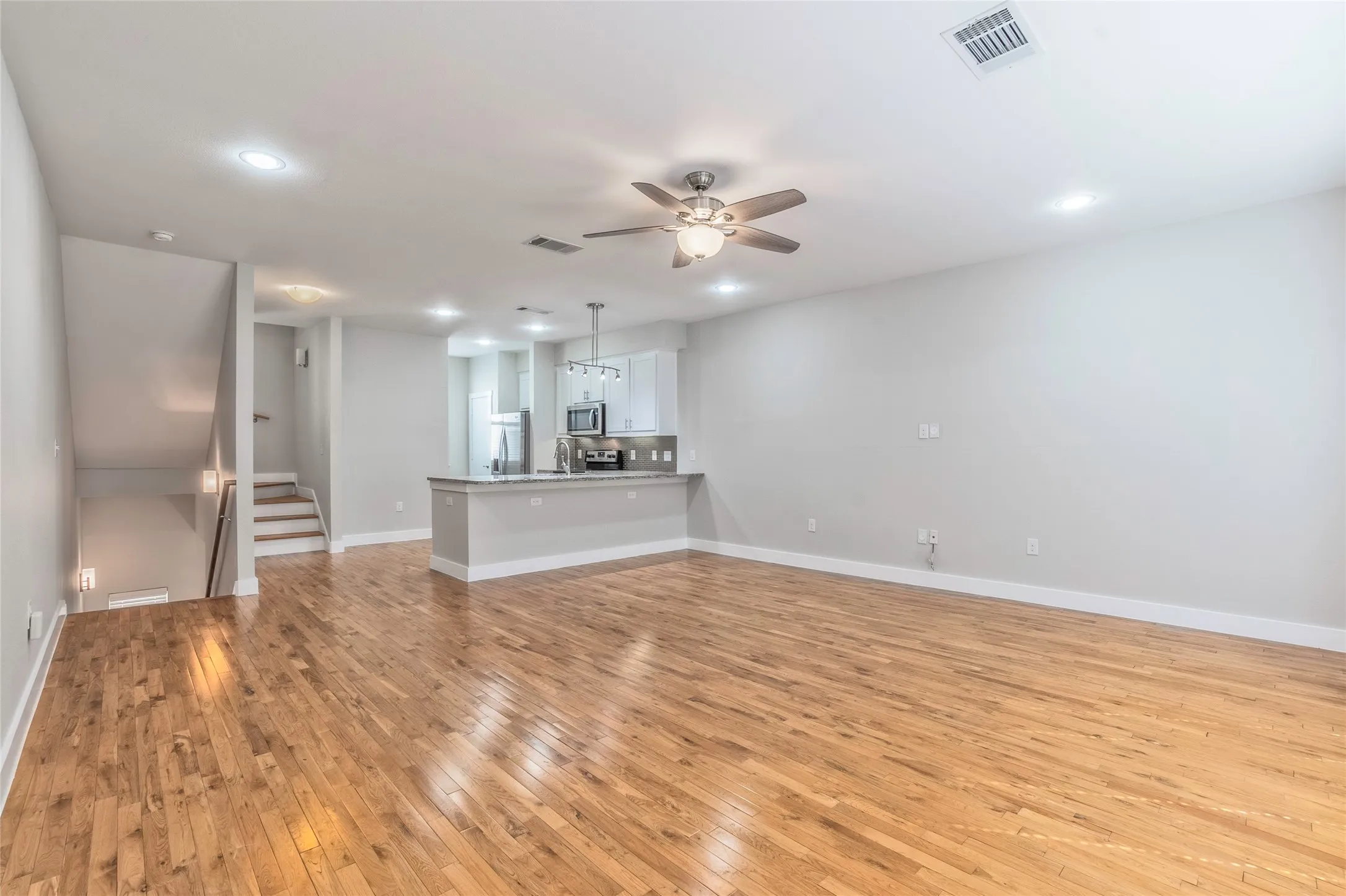 Open-concept living area with wood-finish flooring, recessed lighting, and a ceiling fan
