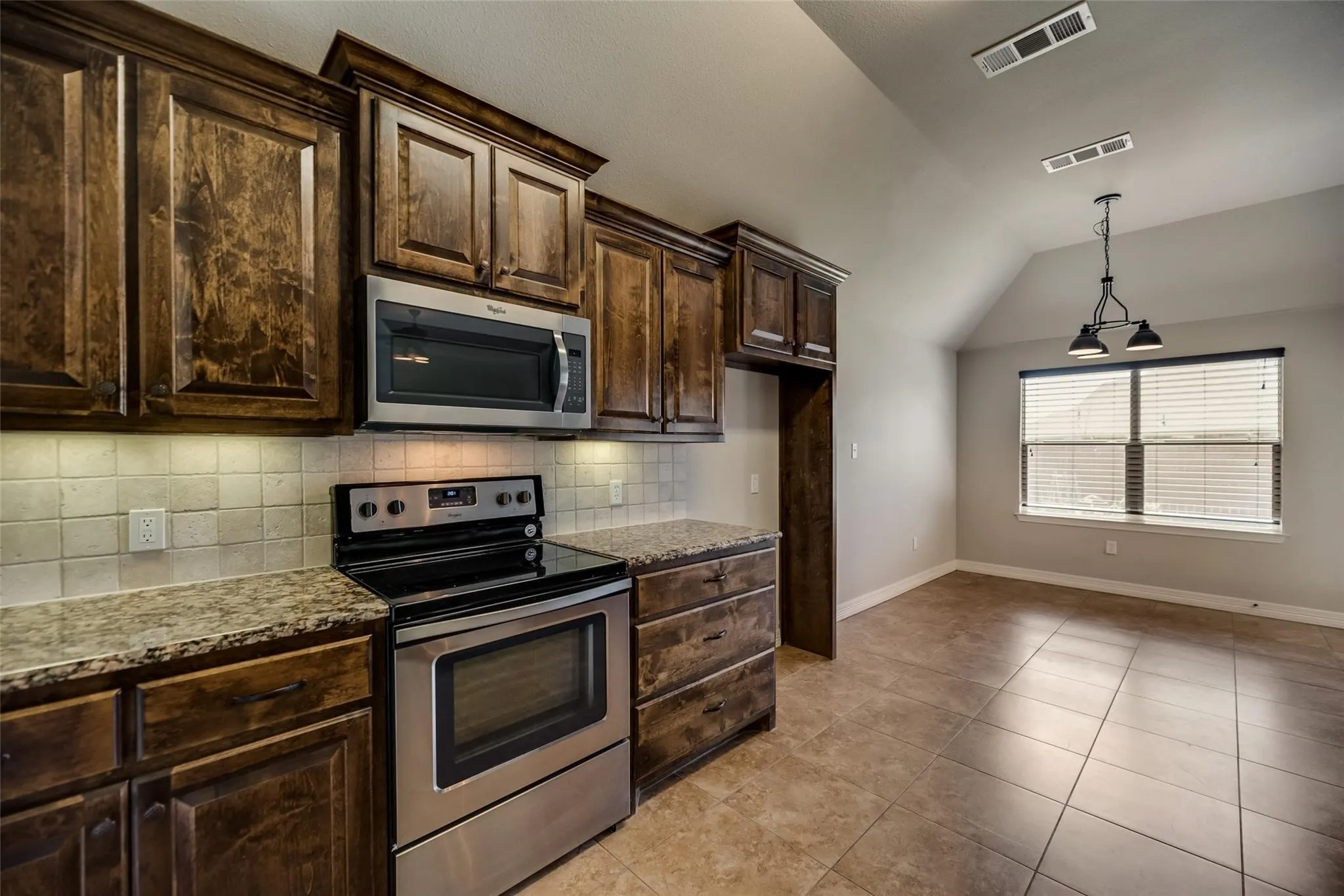 Kitchen featuring wood cabinetry, stainless steel appliances, tile backsplash, and granite countertops