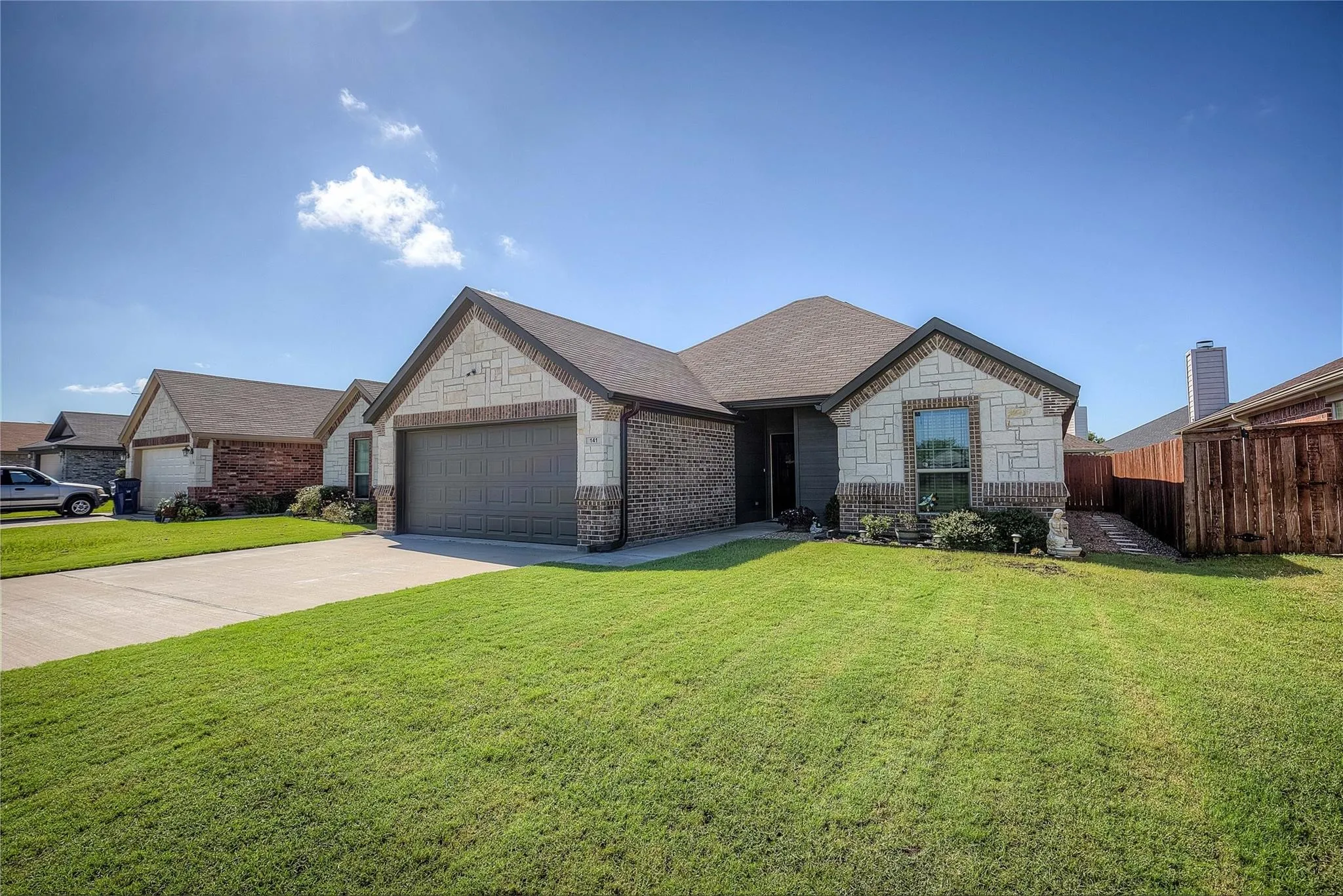 Brick and stone exterior with an attached two-car garage, concrete driveway, and front lawn