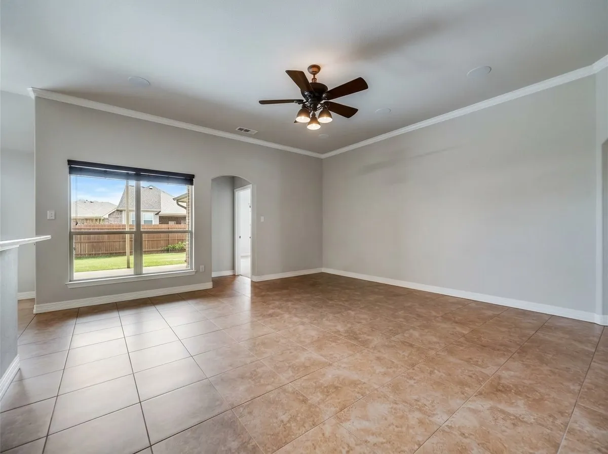 Spacious room featuring tile flooring, a ceiling fan with light fixture, crown molding, and an arched doorway
