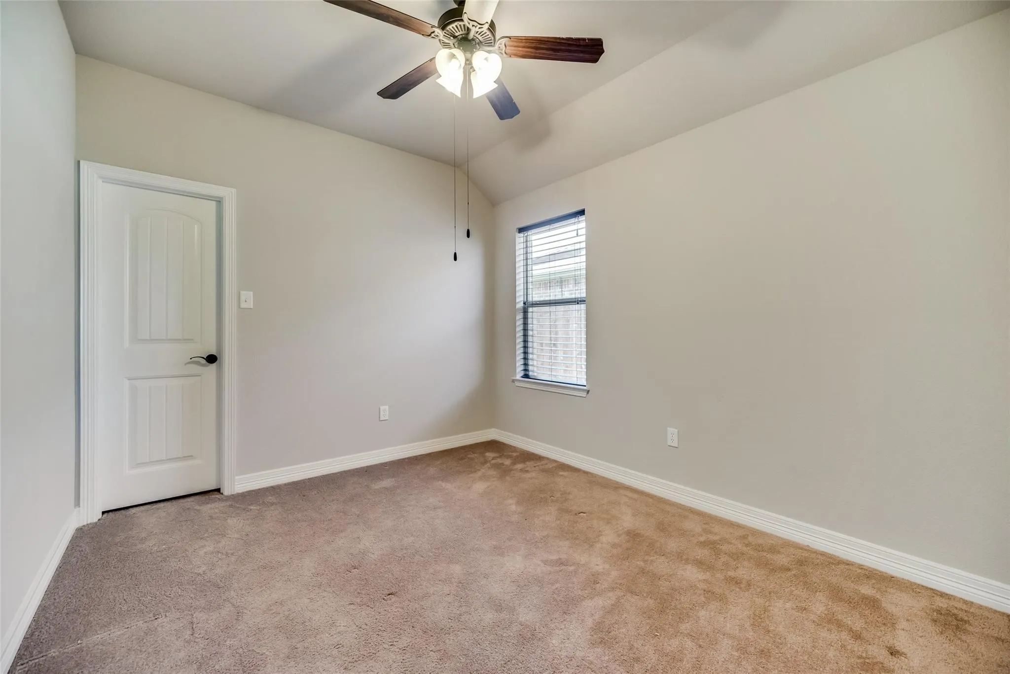 Carpeted room featuring a ceiling fan with light, a window with blinds, and a white paneled door with dark hardware