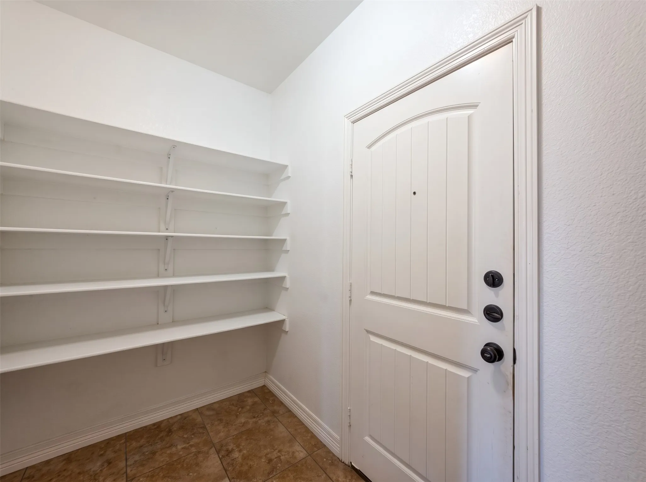 White paneled door with dark hardware, a door frame with decorative trim, and white walls