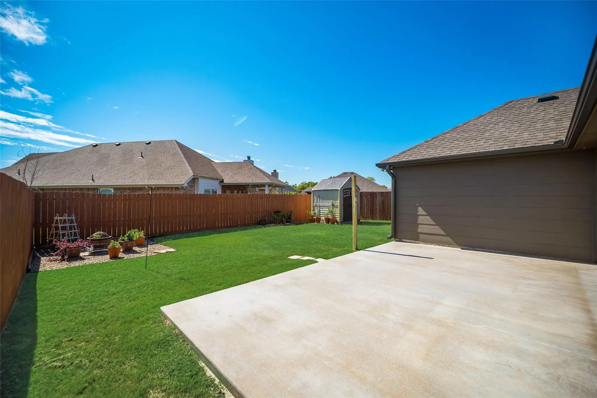 Expansive backyard featuring a privacy fence, concrete patio, and a separate storage structure